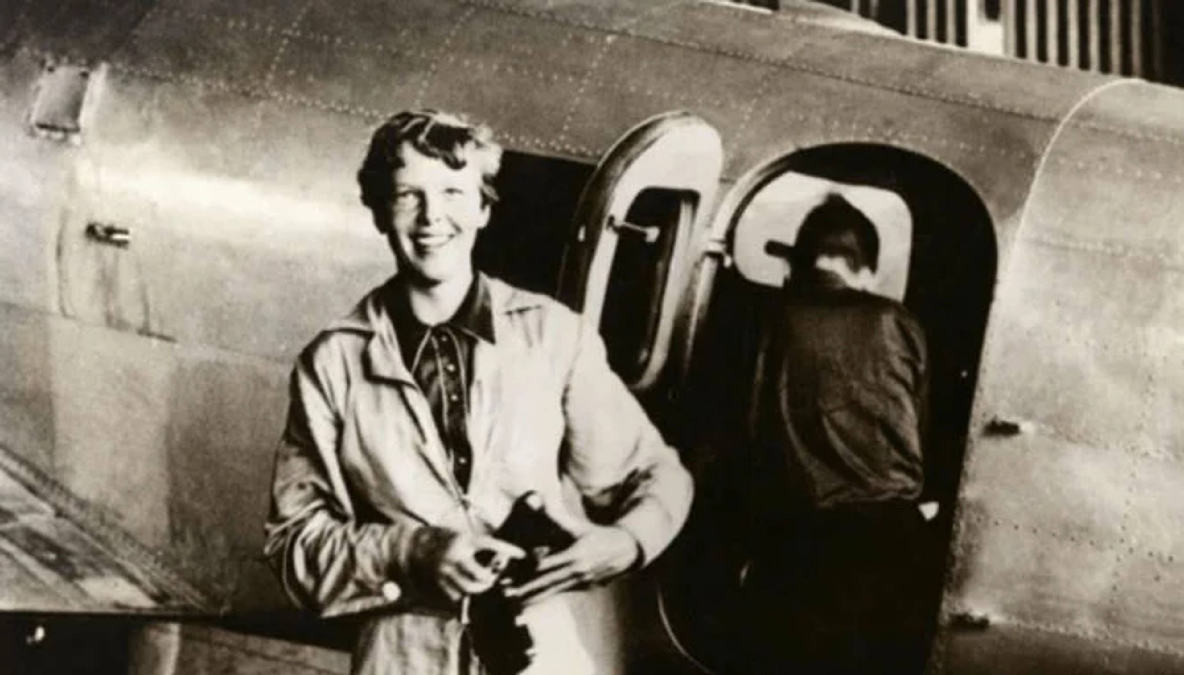 black and white photo of amelia earhart smiling next to plane