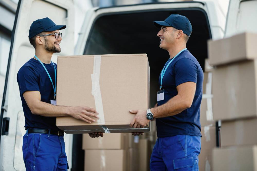 professional movers carrying a box smiling next to van