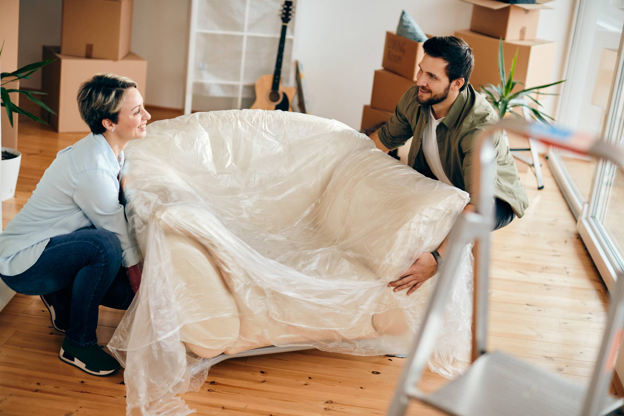 couple lifting wrapped up chair in apartment