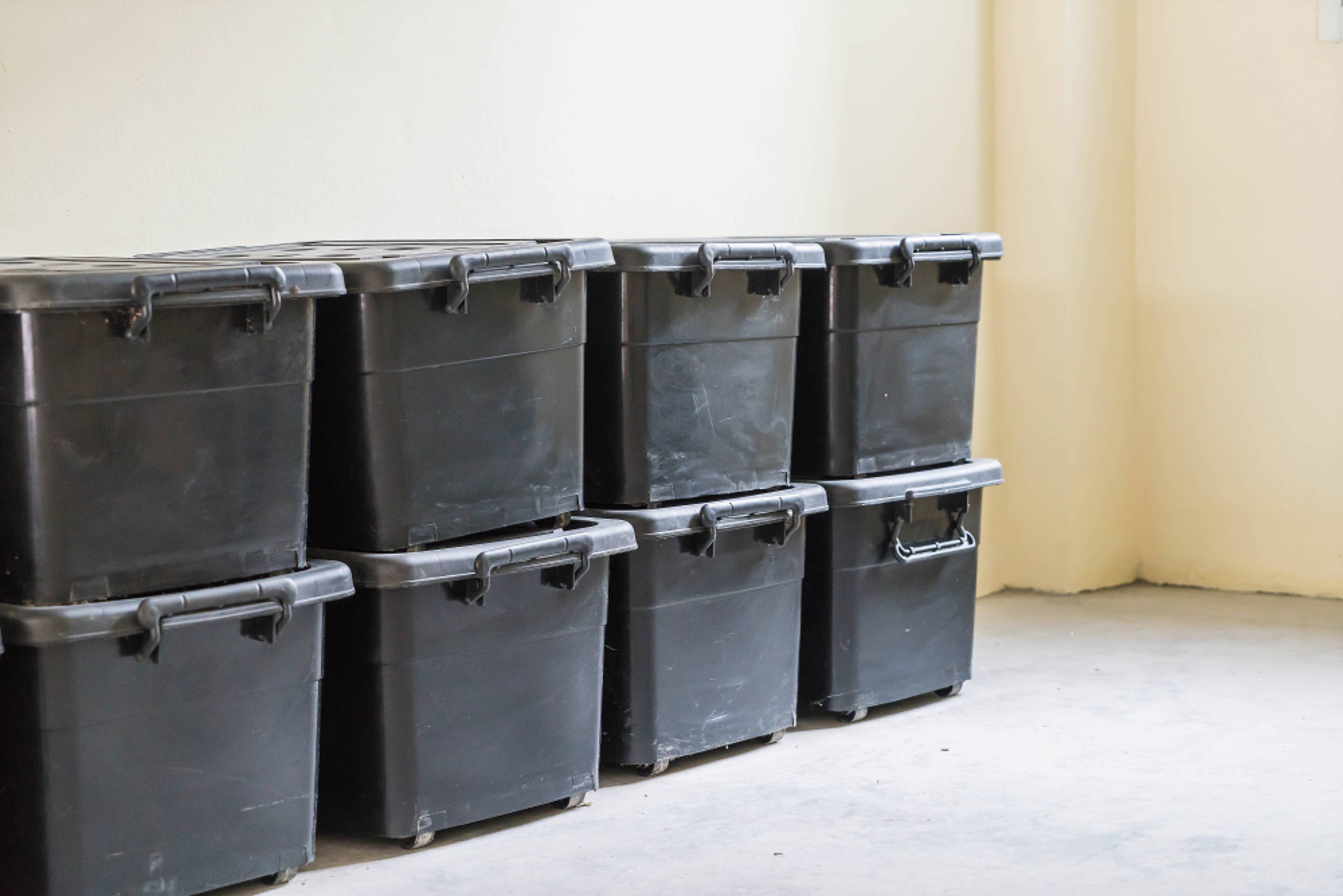 Black plastic containers stacked up against a wall
