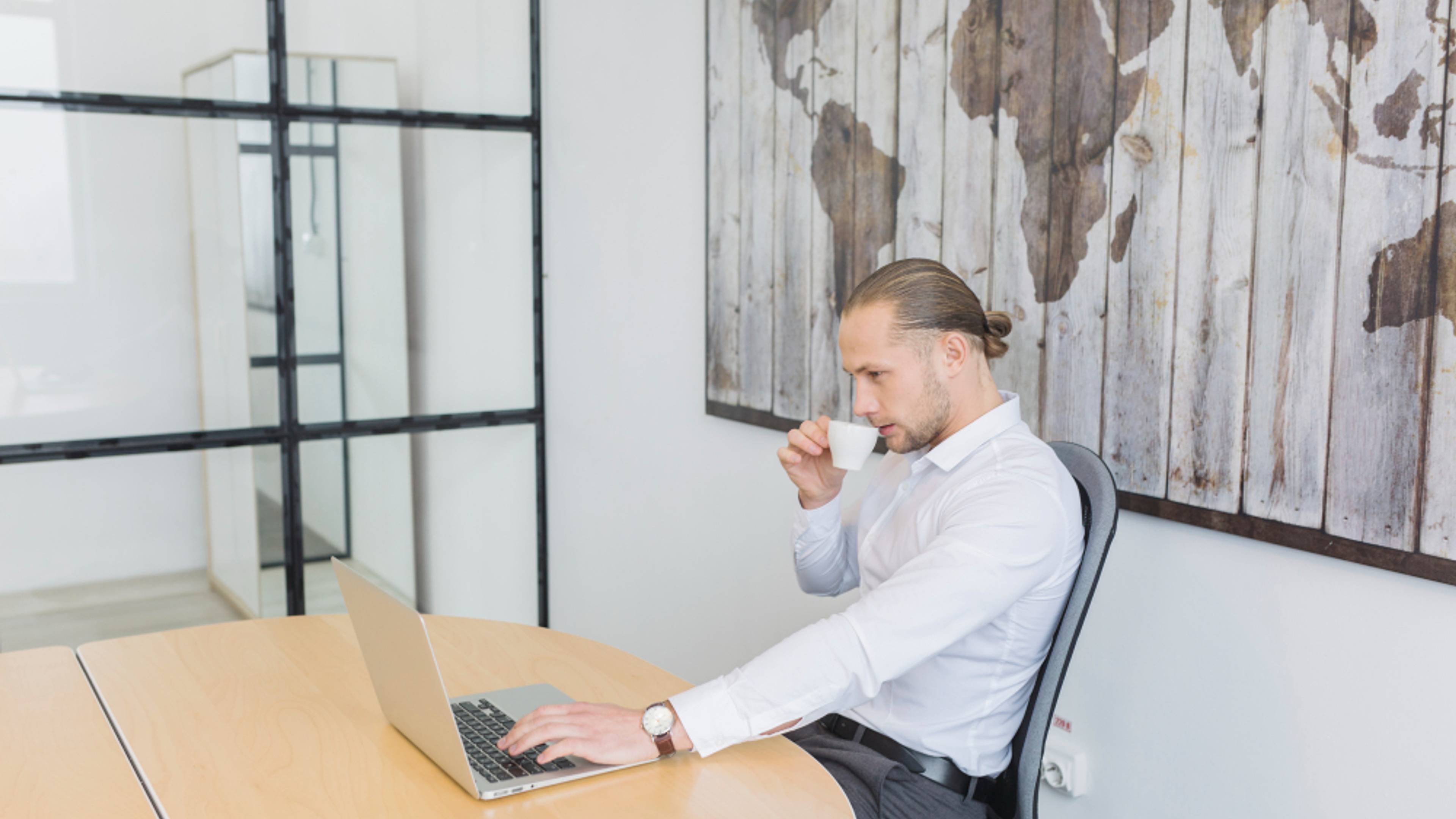 A man sips some coffee as he works in his office