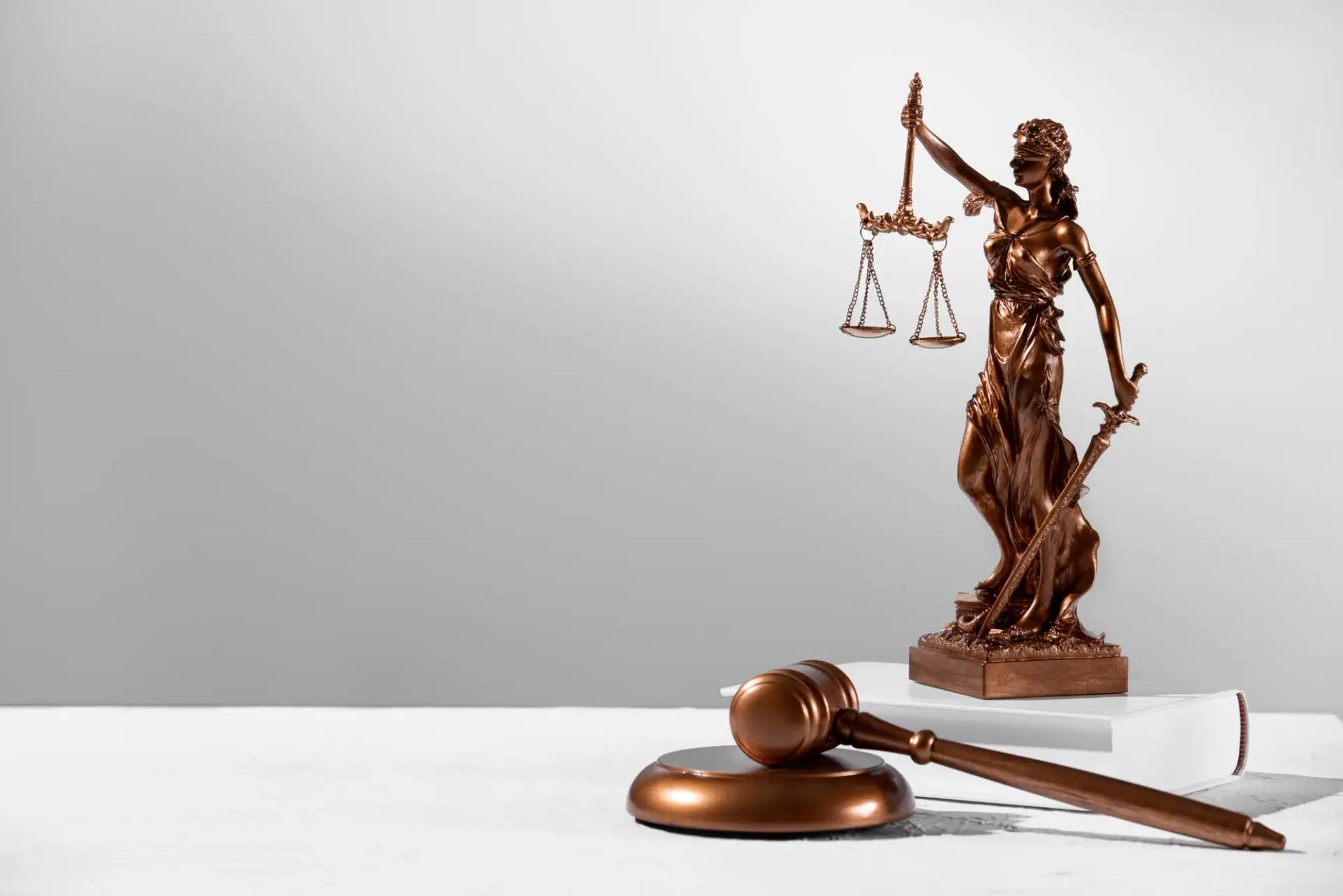 A gavel on a table with a statue of Lady Justice