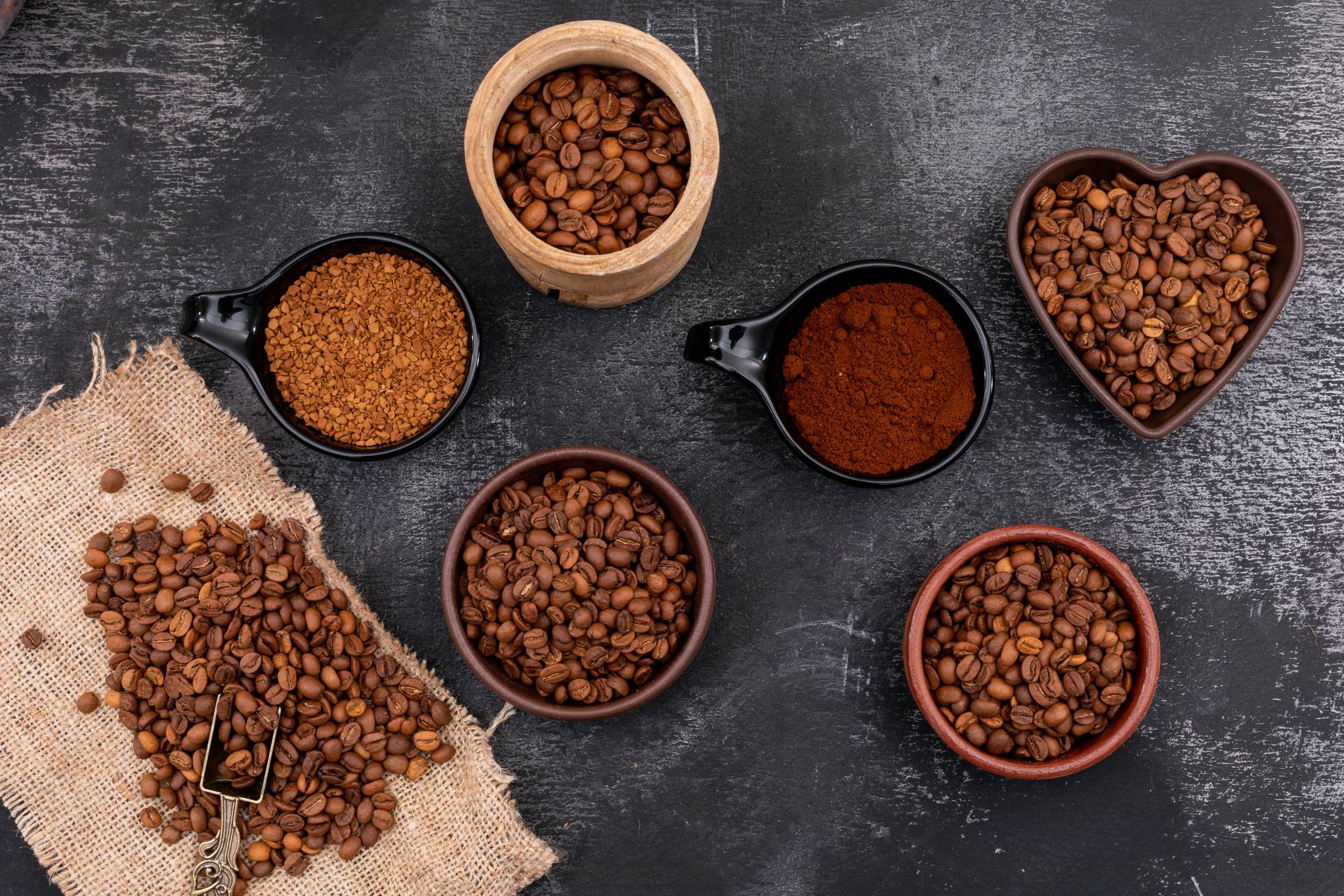 Different kind of coffee in ceramic wood bowl on black wooden surface
