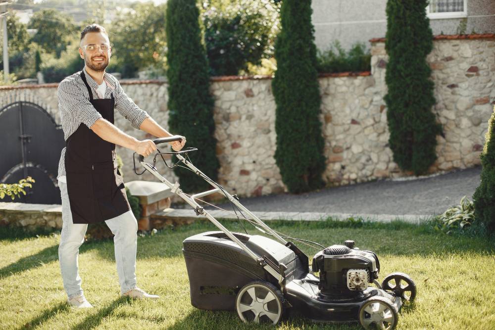 A person mows the lawn while smiling at the camera