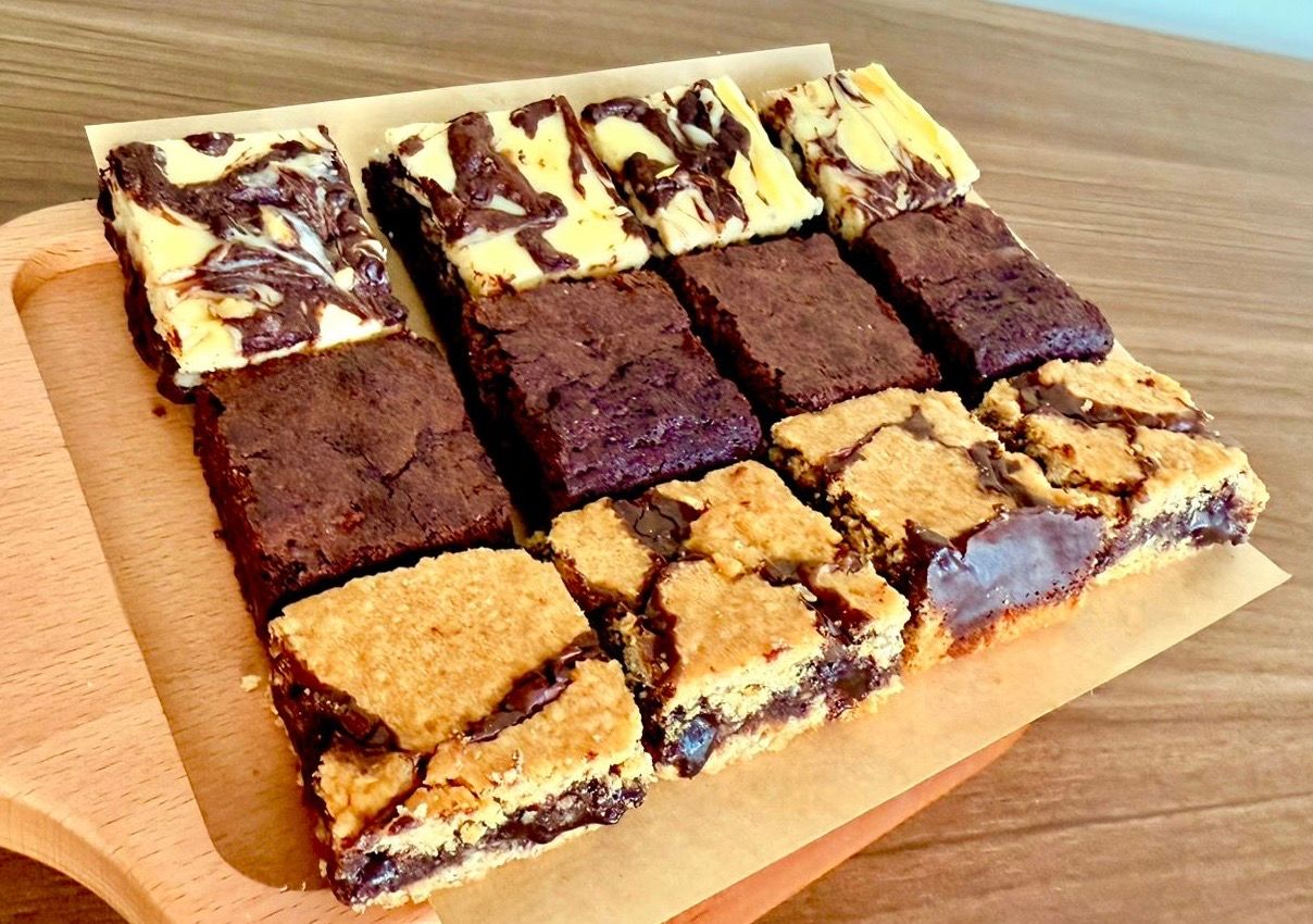 Assorted bars of cheesecake brownies, fudgy chocolate brownies, and chewy revel bars.