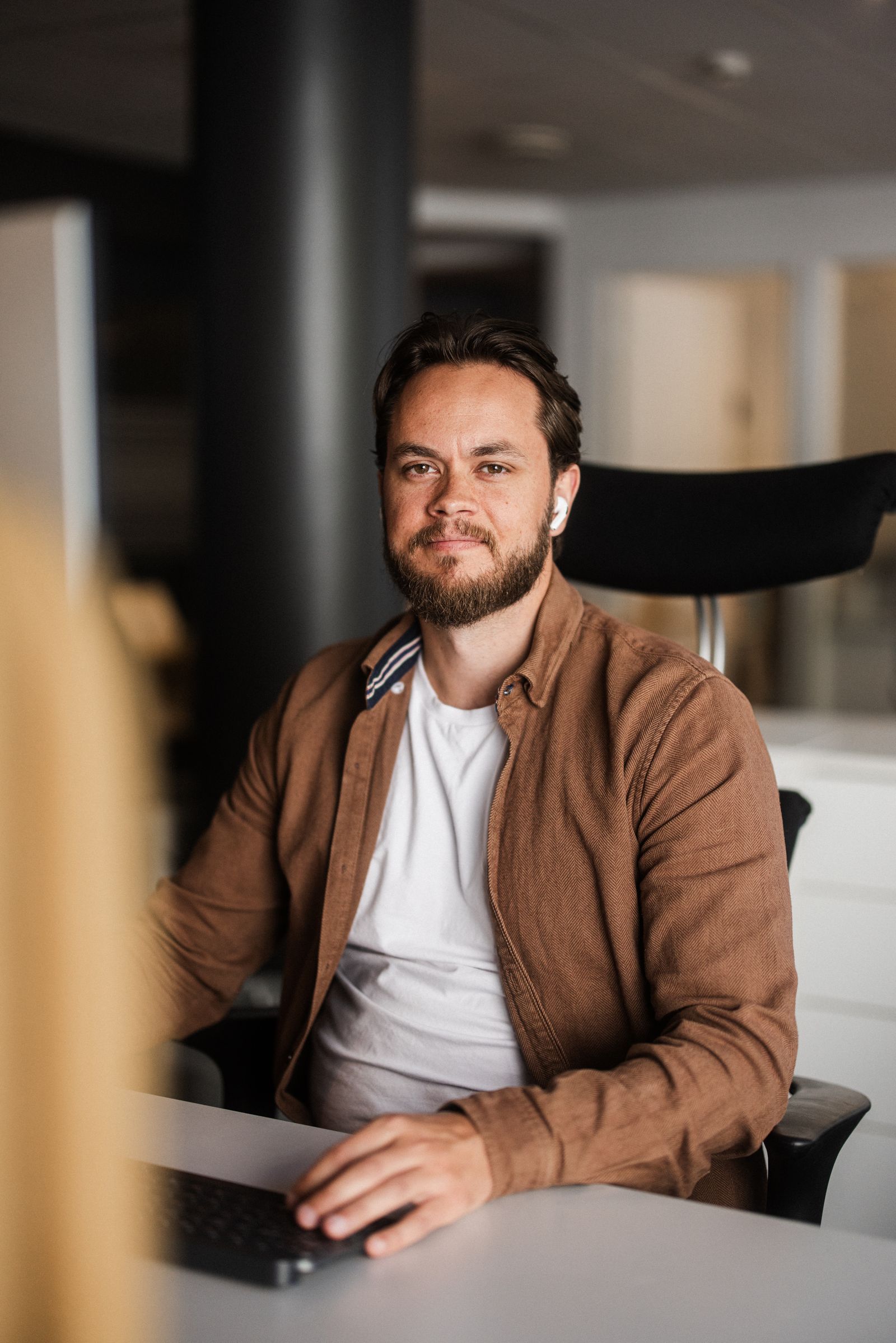 Mats sitter på arbeidsplassen med hendene på tastaturet. Han ser rett i kamera med et smil.