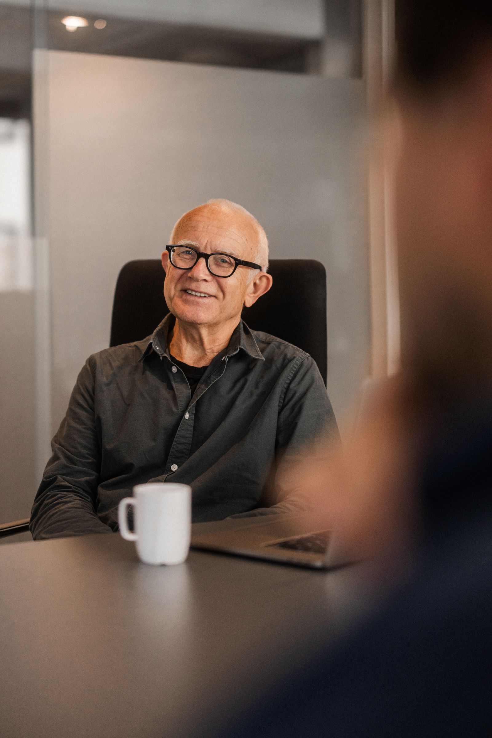Terje sitter ved et bord med laptop og kaffekopp og smiler til kamera.