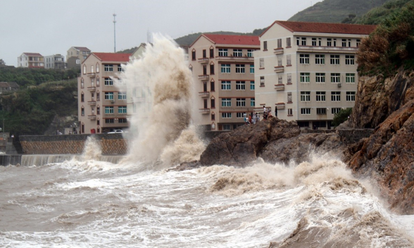 Storm surge crashing against a seawall and apartment buildings on a rocky East China coast during a typhoon.