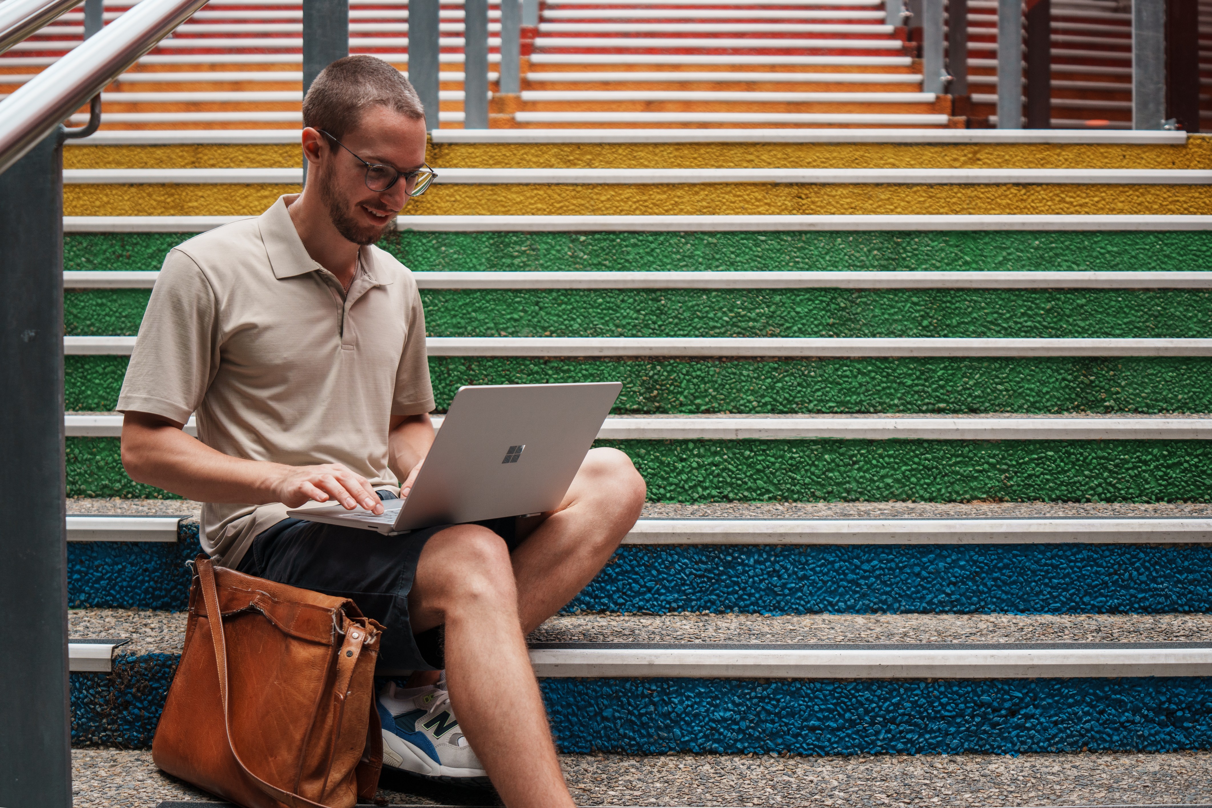 student sitting on rainbow-coloured stairs, looking at laptop