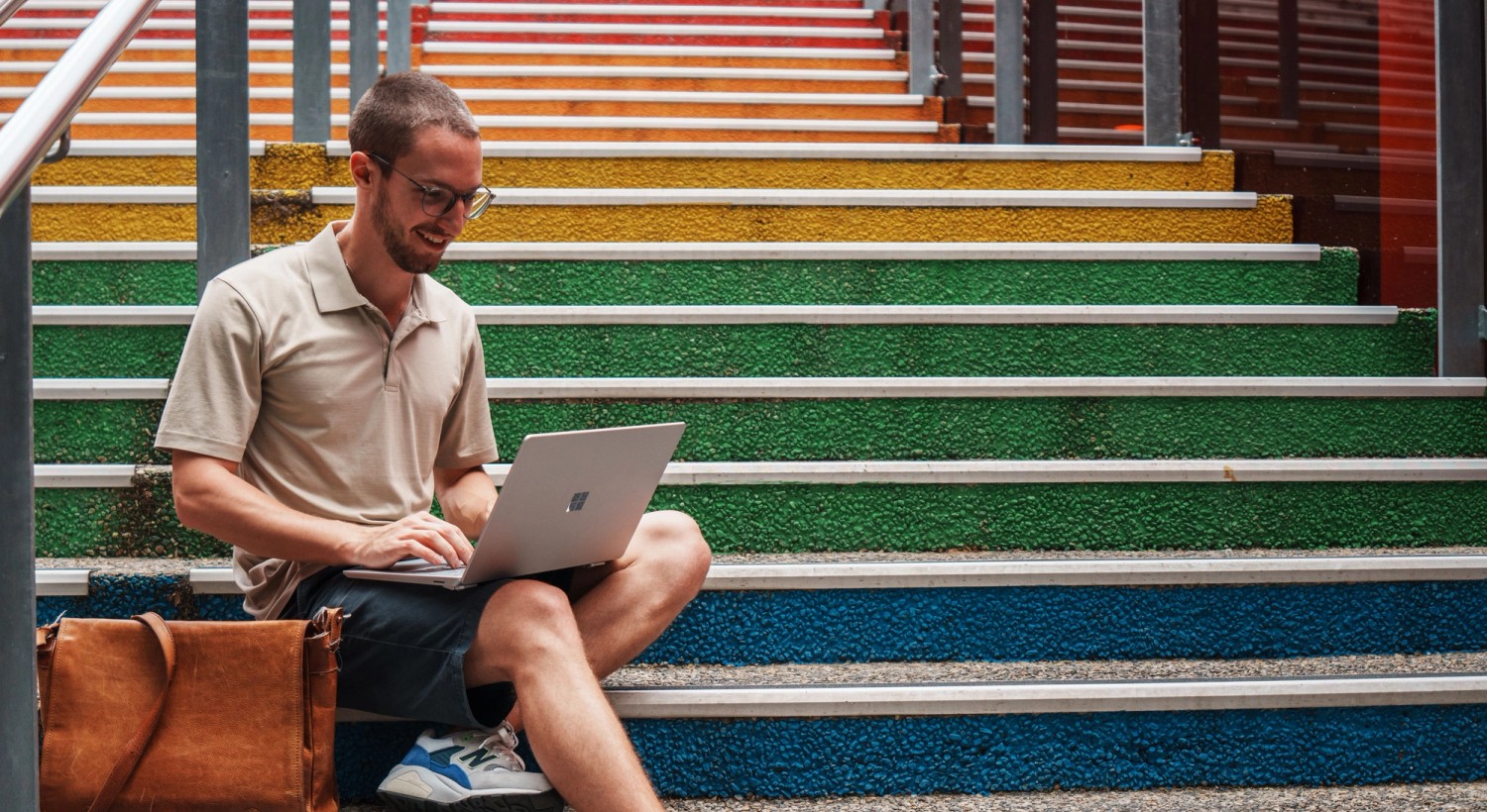 Student sitting on rainbow coloured stairs, looking at laptop