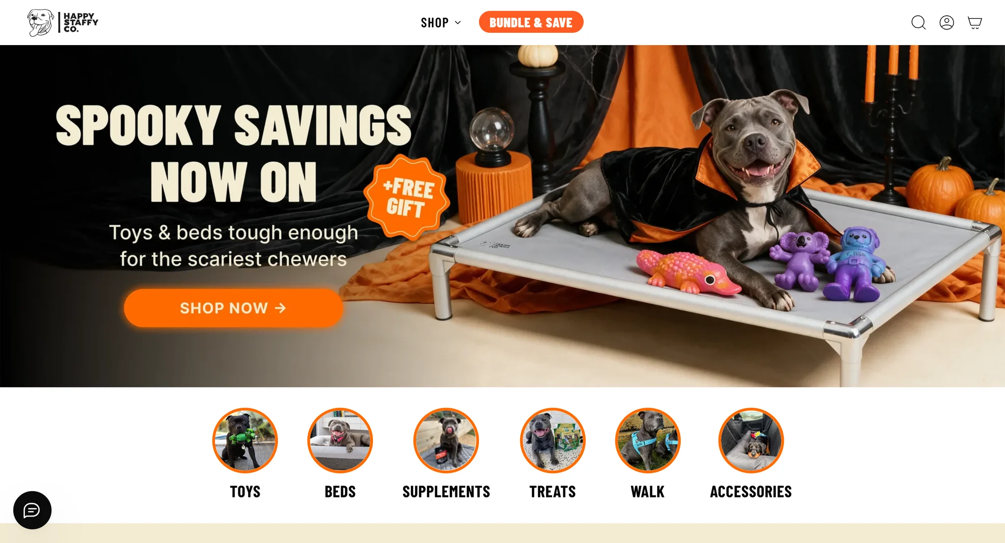 Happy Staffy Co homepage hero with the headline "Spooky savings now on", a Staffy in a Halloween cape on a raised dog bed with Chewzilla toys, and round links to toys, beds, supplements, treats, walk and accessories