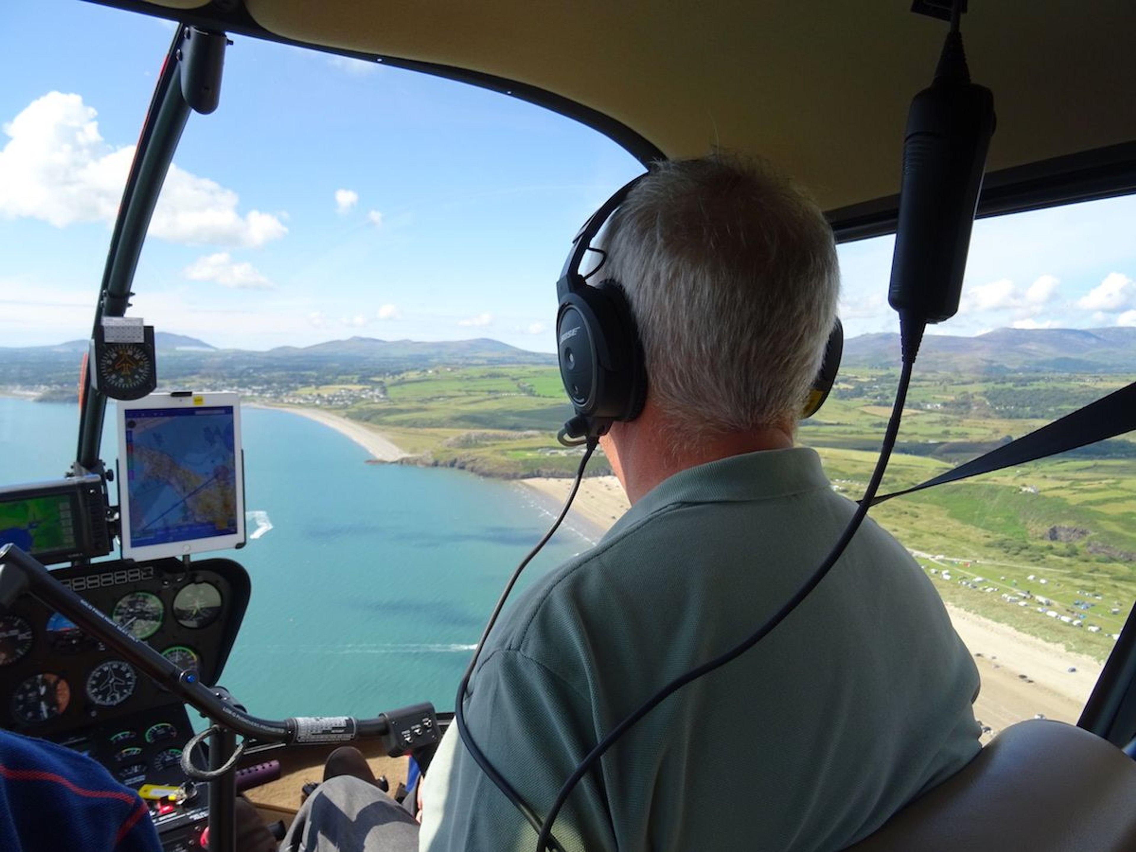 Pilot flying a helicopter along a coastline of beaches and hills