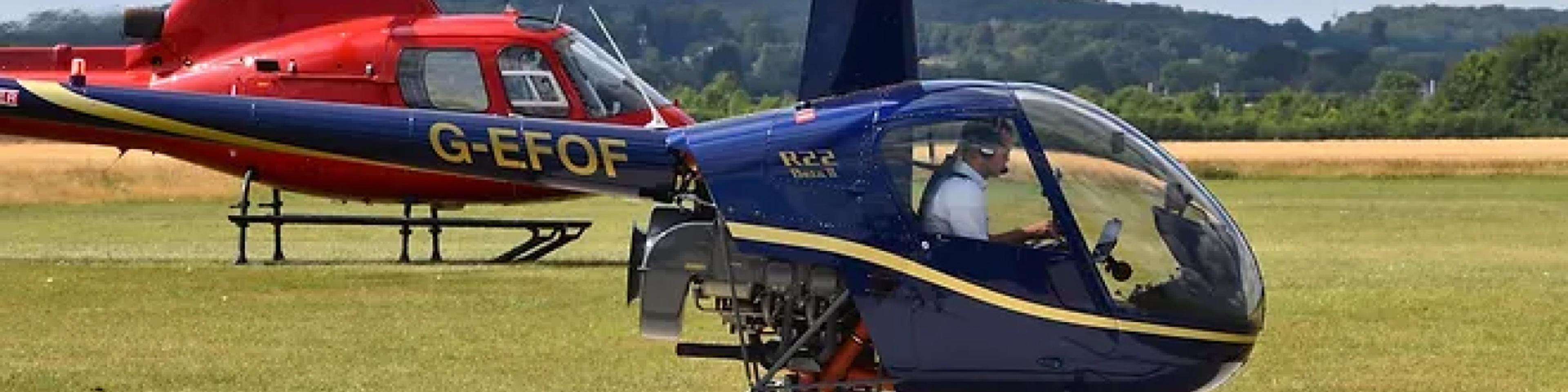 Robinson R22 and a red helicopter on the grass ready for trial lessons
