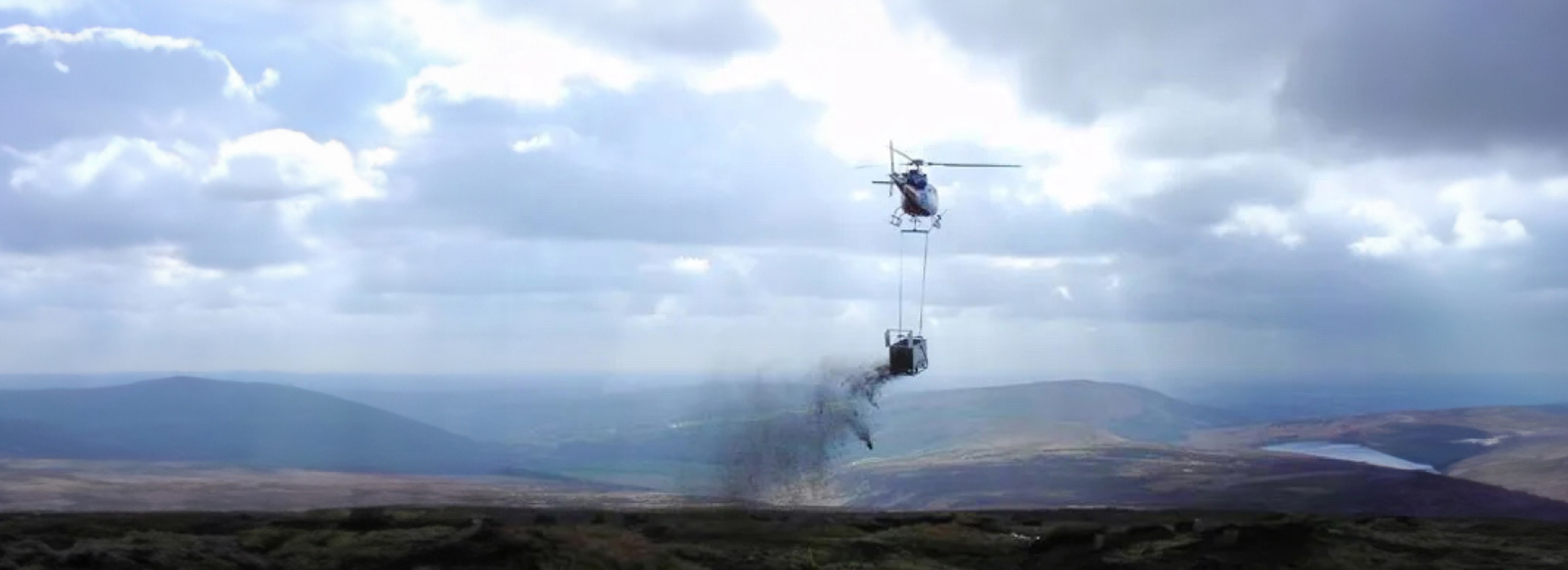 Helicopter lifting an underslung load over moorland