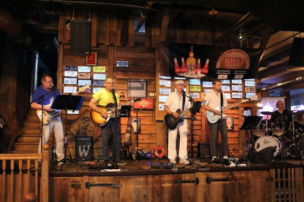 Die Original Austrobuam spielen gemeinsam vor der Holzwand mit Nummernschildern im Saloon.