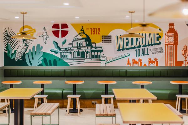 A bright cafe, with drawings and color on the walls, empty tables ready for customers