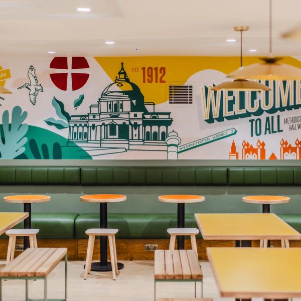 A bright cafe, with drawings and color on the walls, empty tables ready for customers