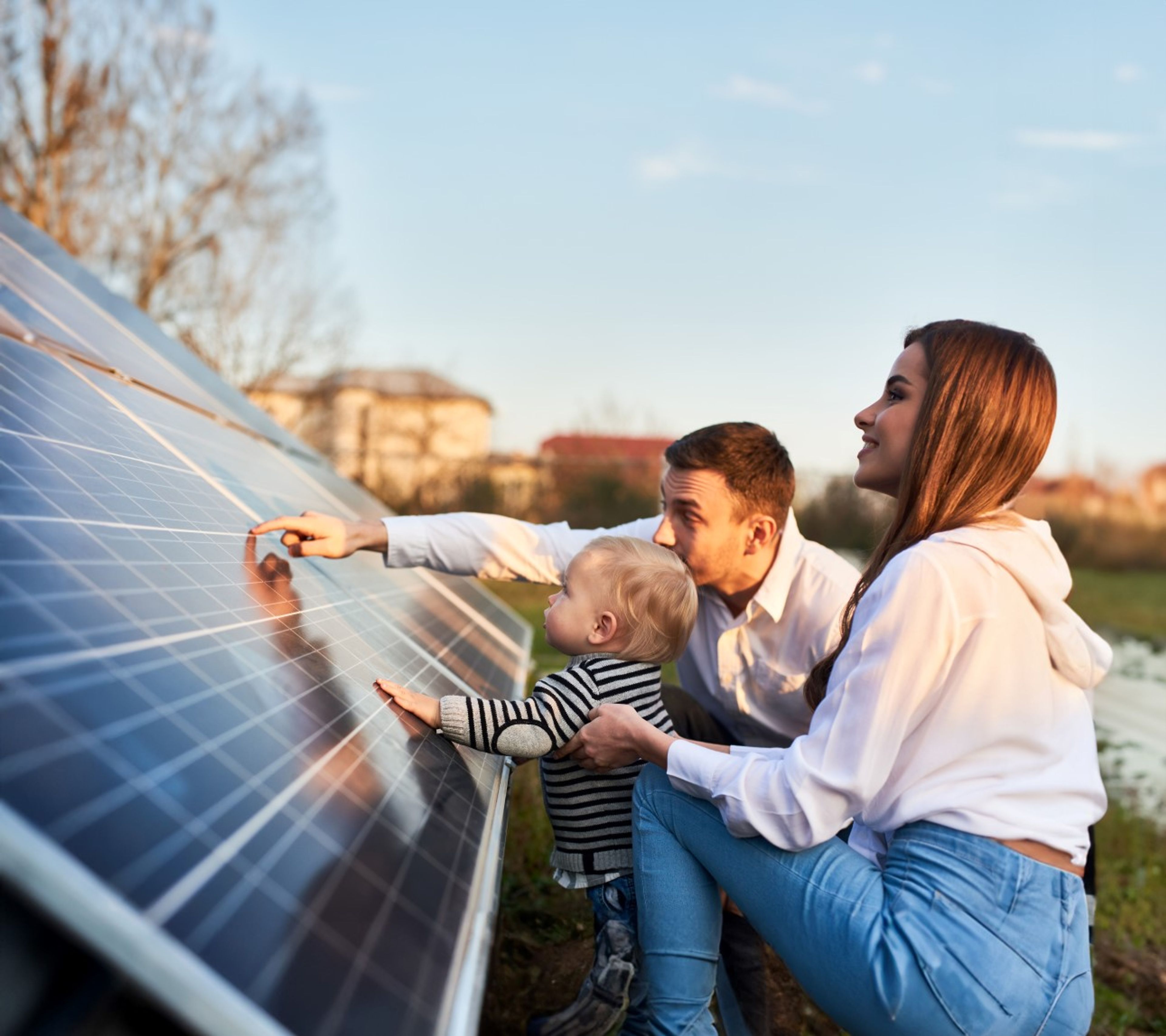 Jong koppel met kindje zit geknield bij zonnepanelen. Papa en de peuter hebben hun hand op het paneel.