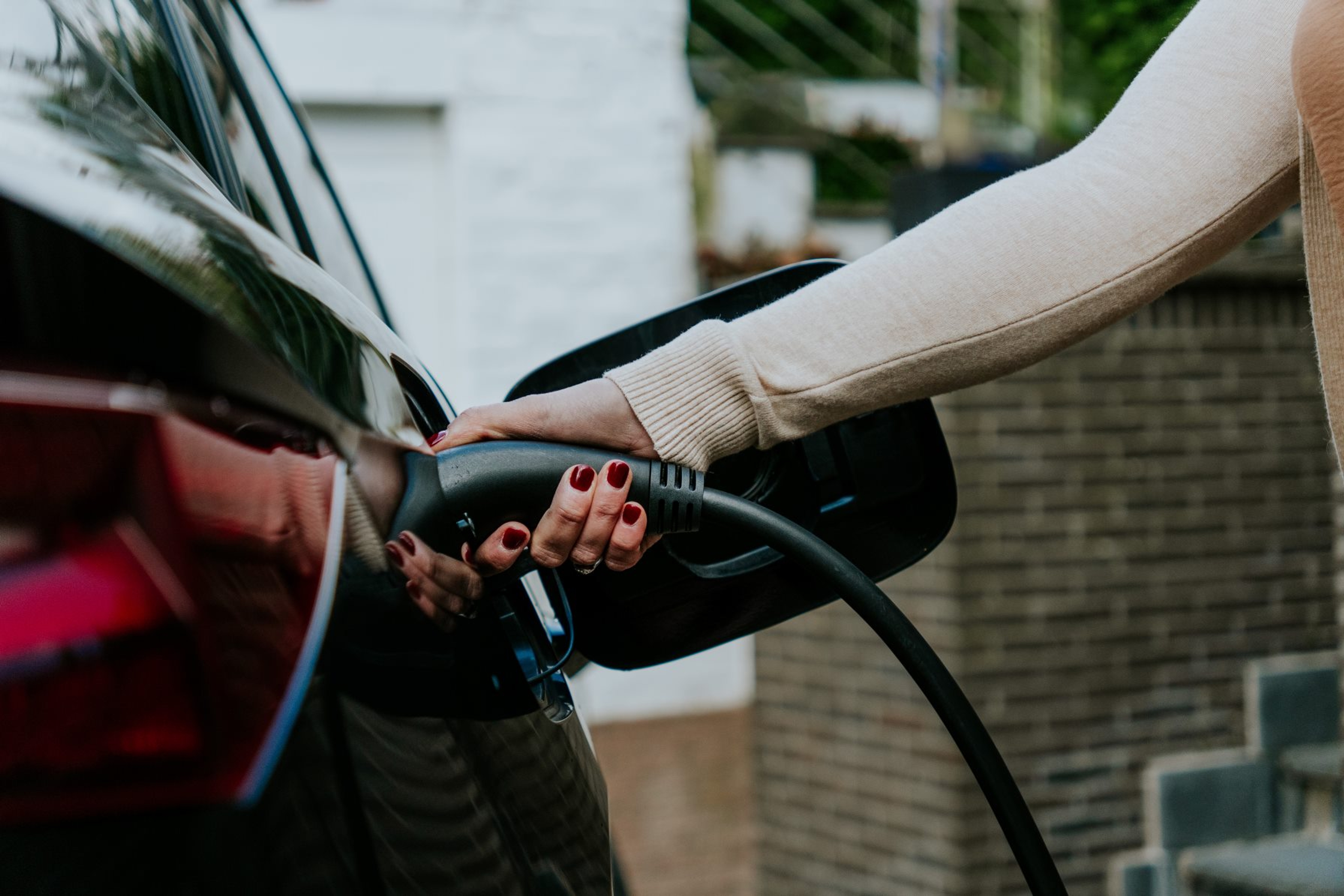 Dame op de oprit laadt haar elektrische wagen op, van de dame zien we enkel haar hand.