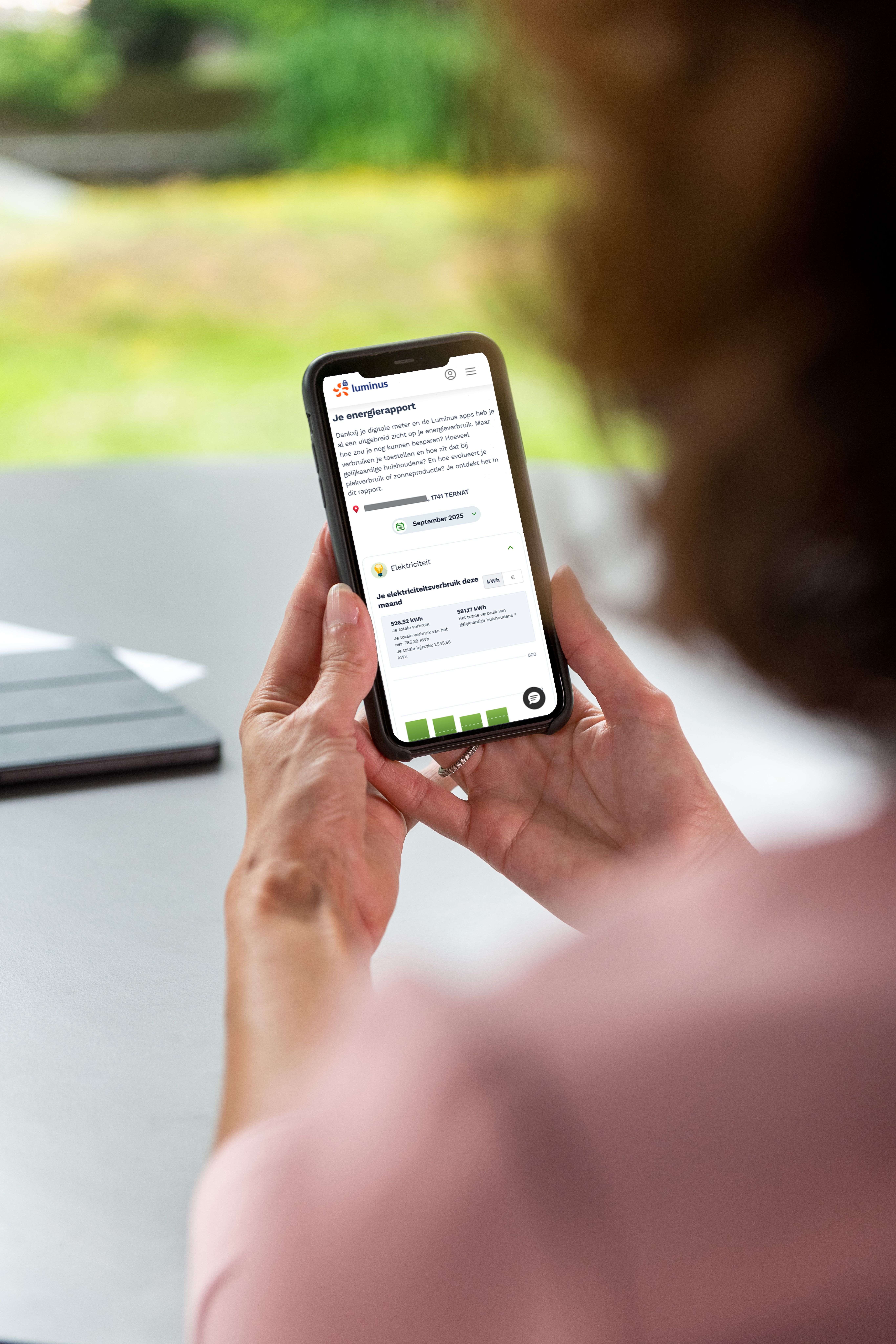Handen van een dame houden een smartphone vast, daarop een scherm van My Luminus met 'Je energierapport'.