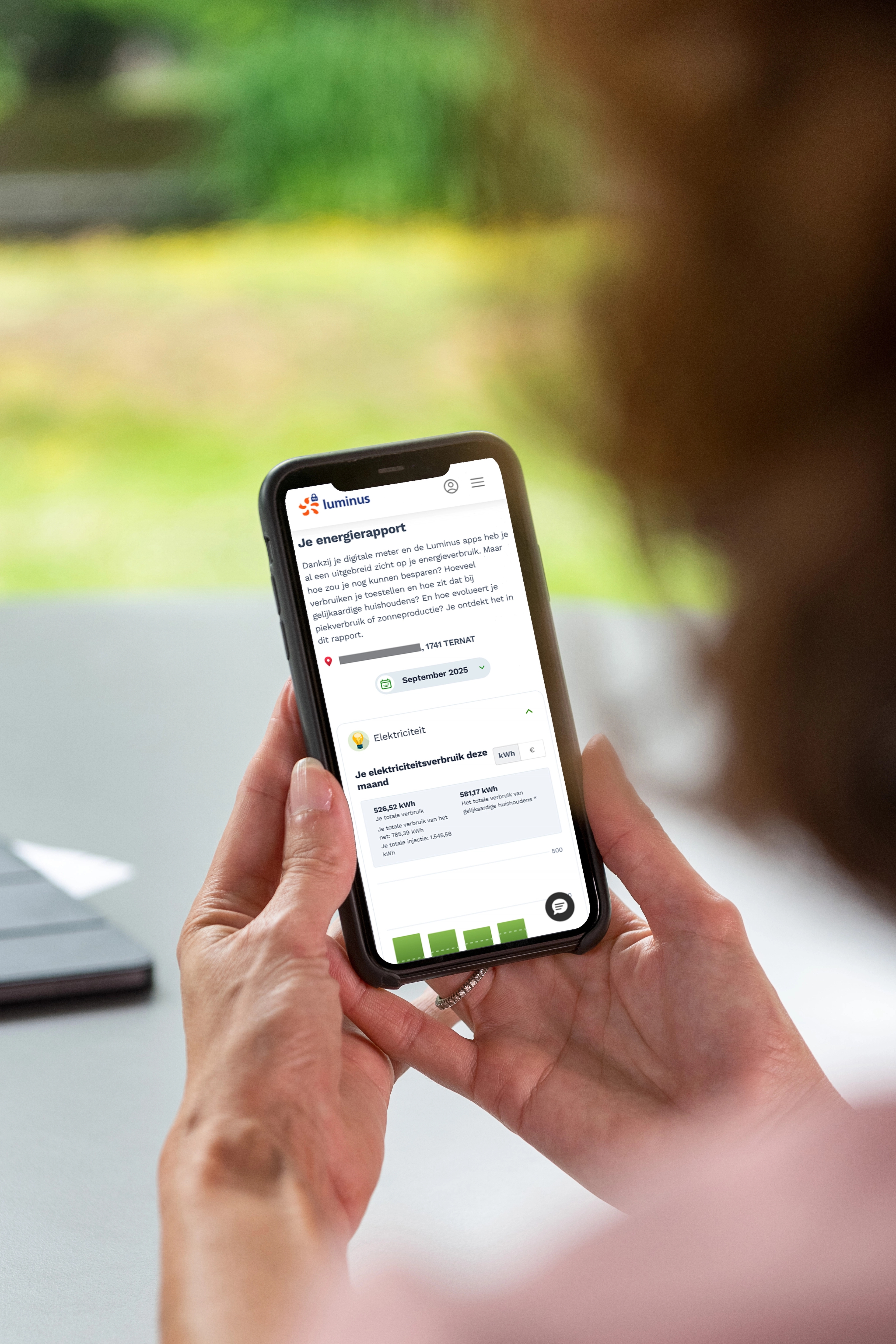 Handen van een dame houden een smartphone vast, daarop een scherm van My Luminus met 'Je energierapport'.
