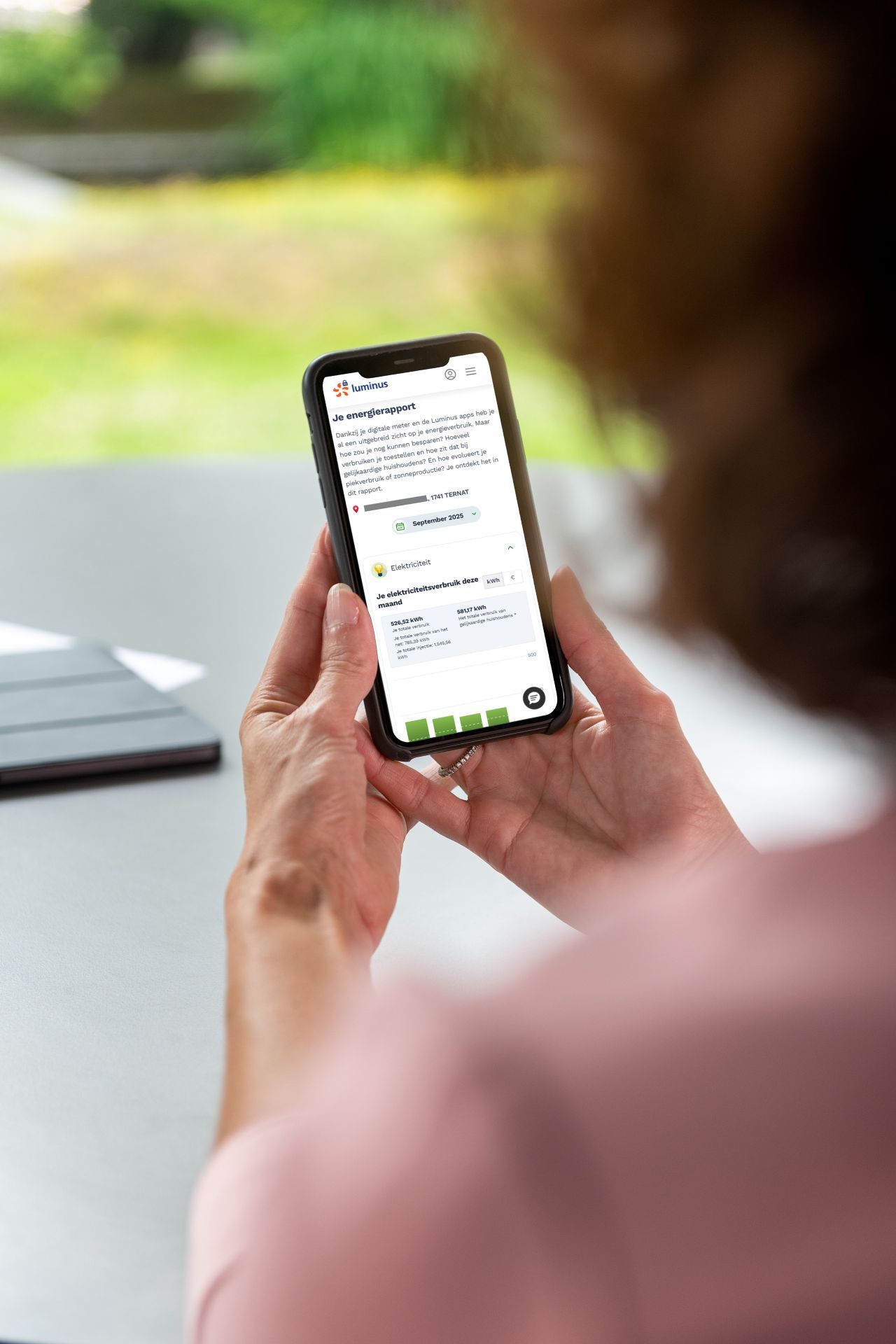Handen van een dame houden een smartphone vast, daarop een scherm van My Luminus met 'Je energierapport'.