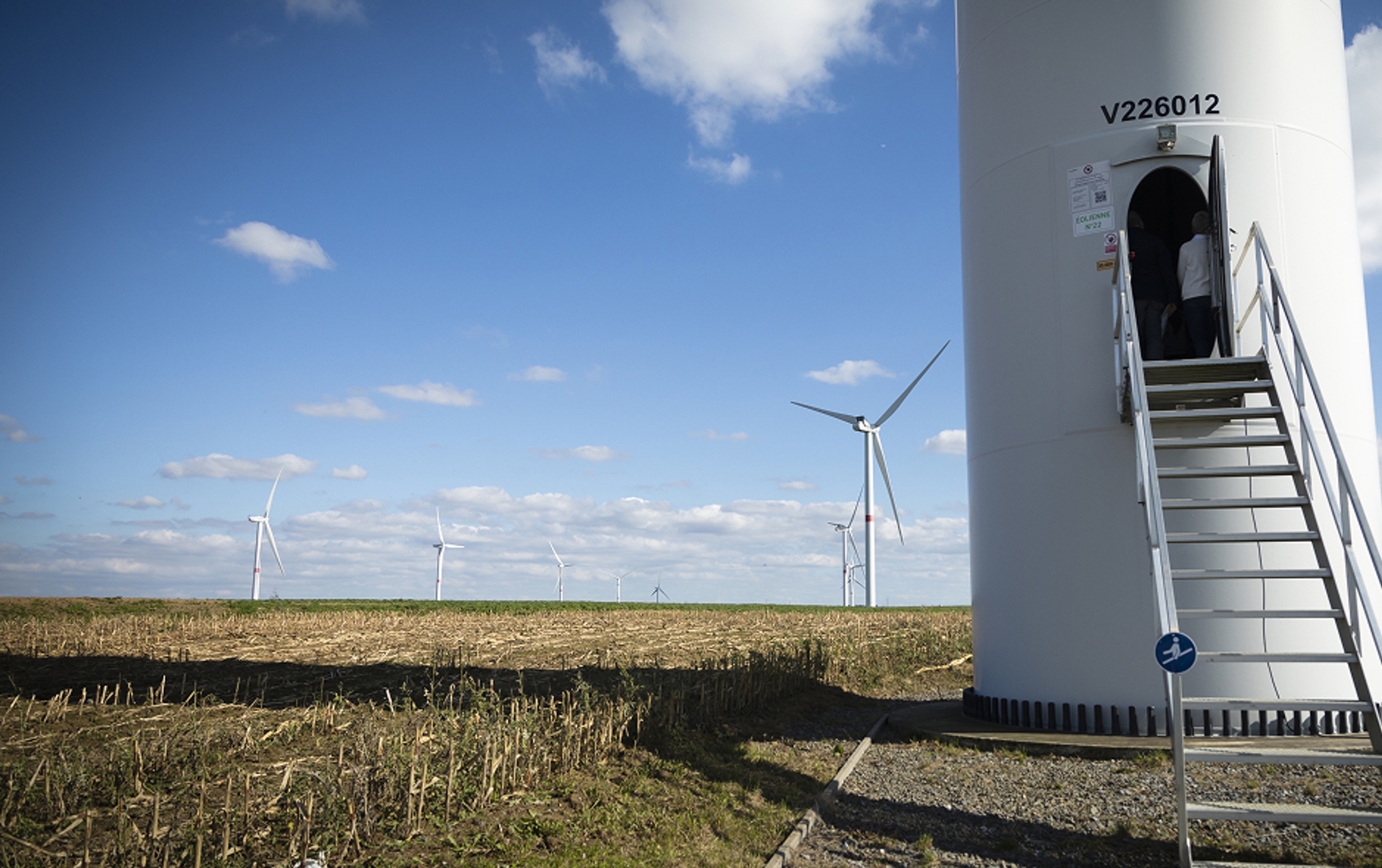 Windturbine, gezien aan de voet met trap en deur, meerdere windturbines in de verte.