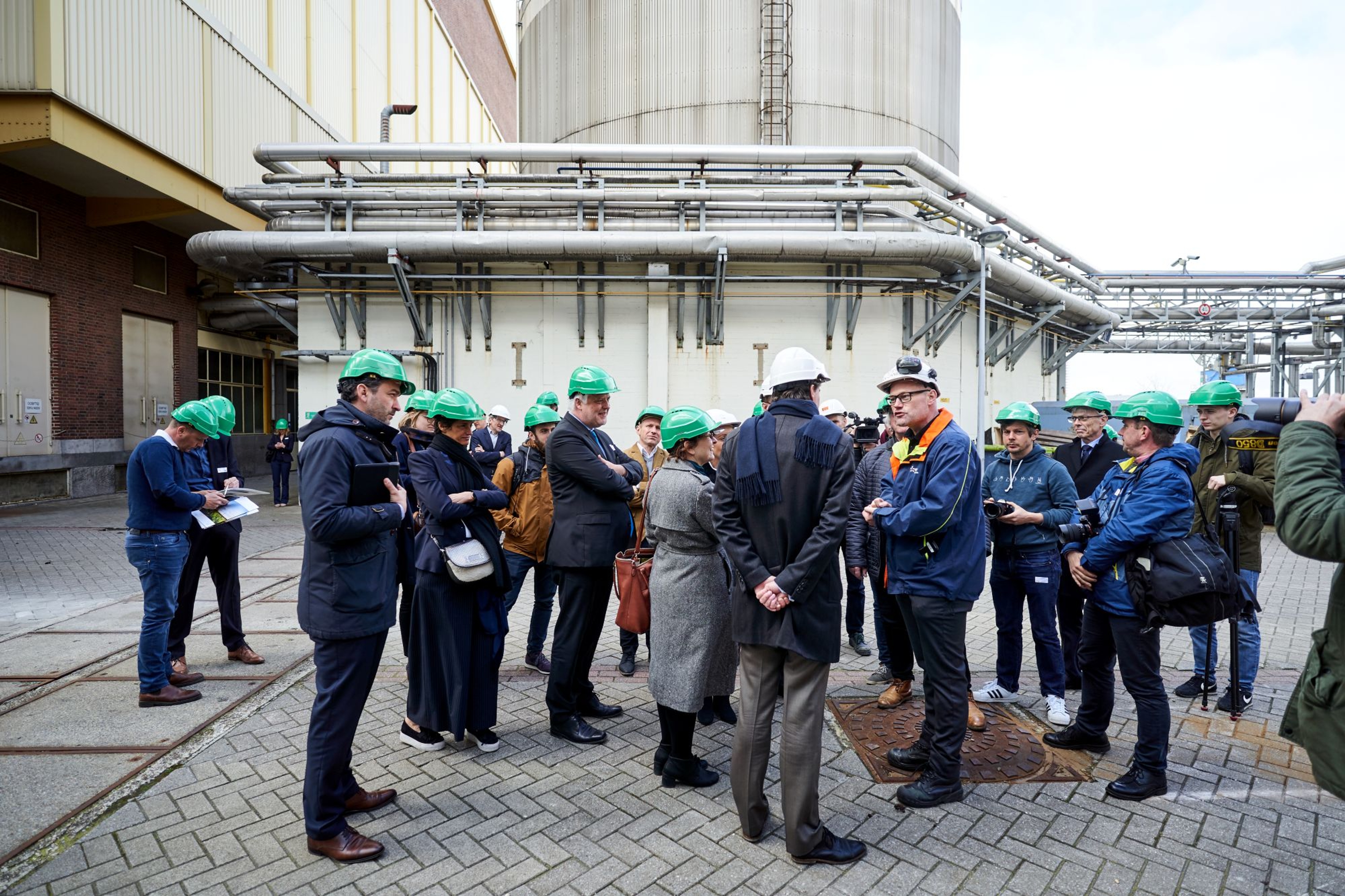 Een groep van 20-tal personen met groene of witte helm op krijgt uitleg van een gids in een energiecentrale.
