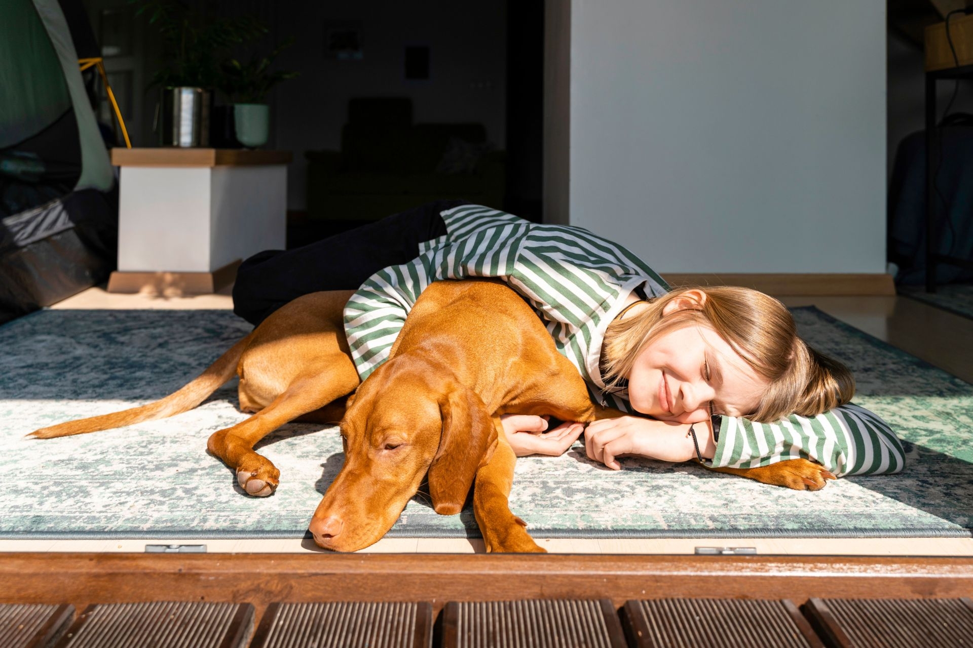 meisje en cognackleurige hond liggen in living op het tapijt te genieten van de zon.
