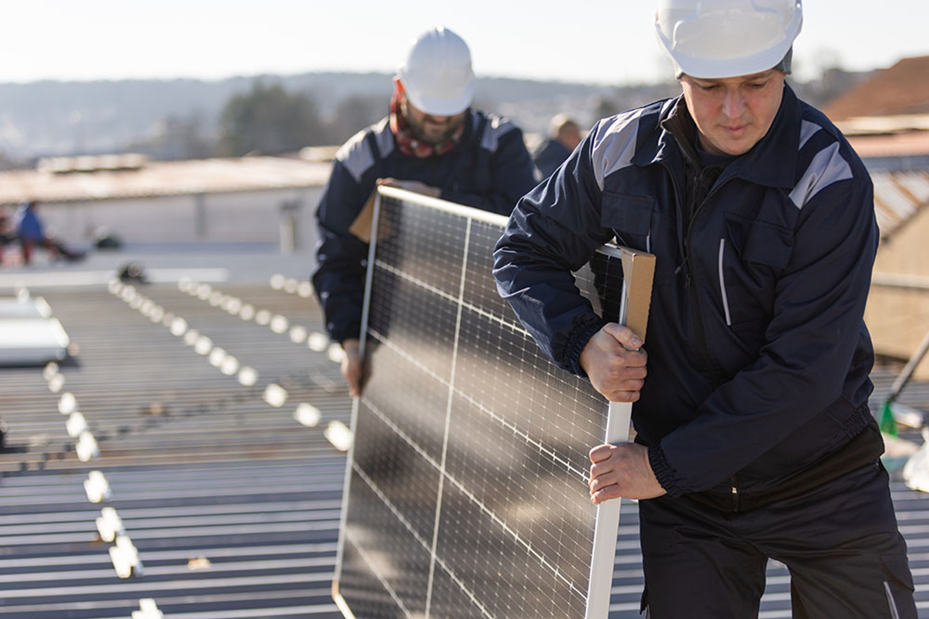 2 mannen dragen zonnepaneel dat ze gaan installeren op een industrieel dak 