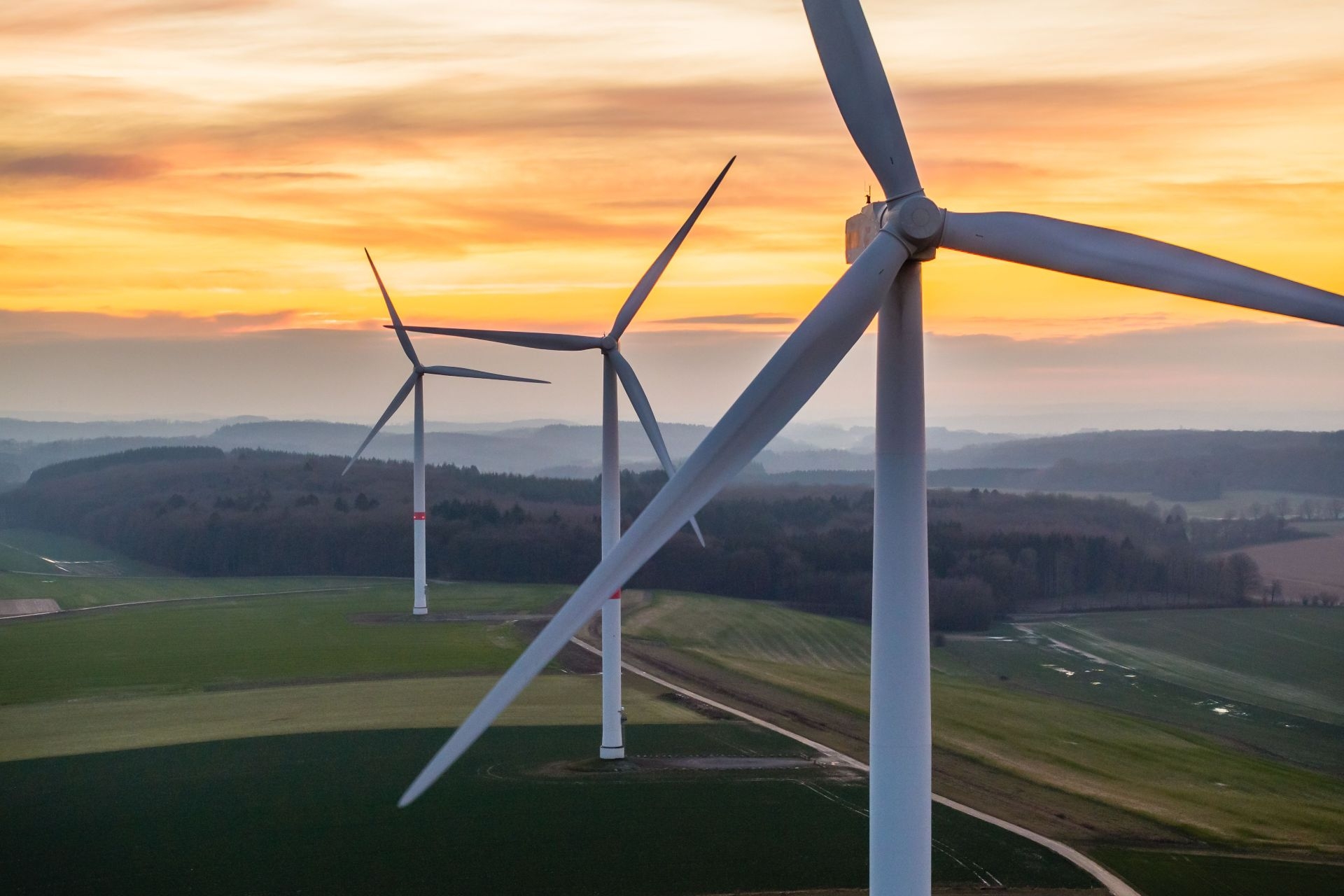 Trois éoliennes alignées dans un paysage vallonné au coucher du soleil
