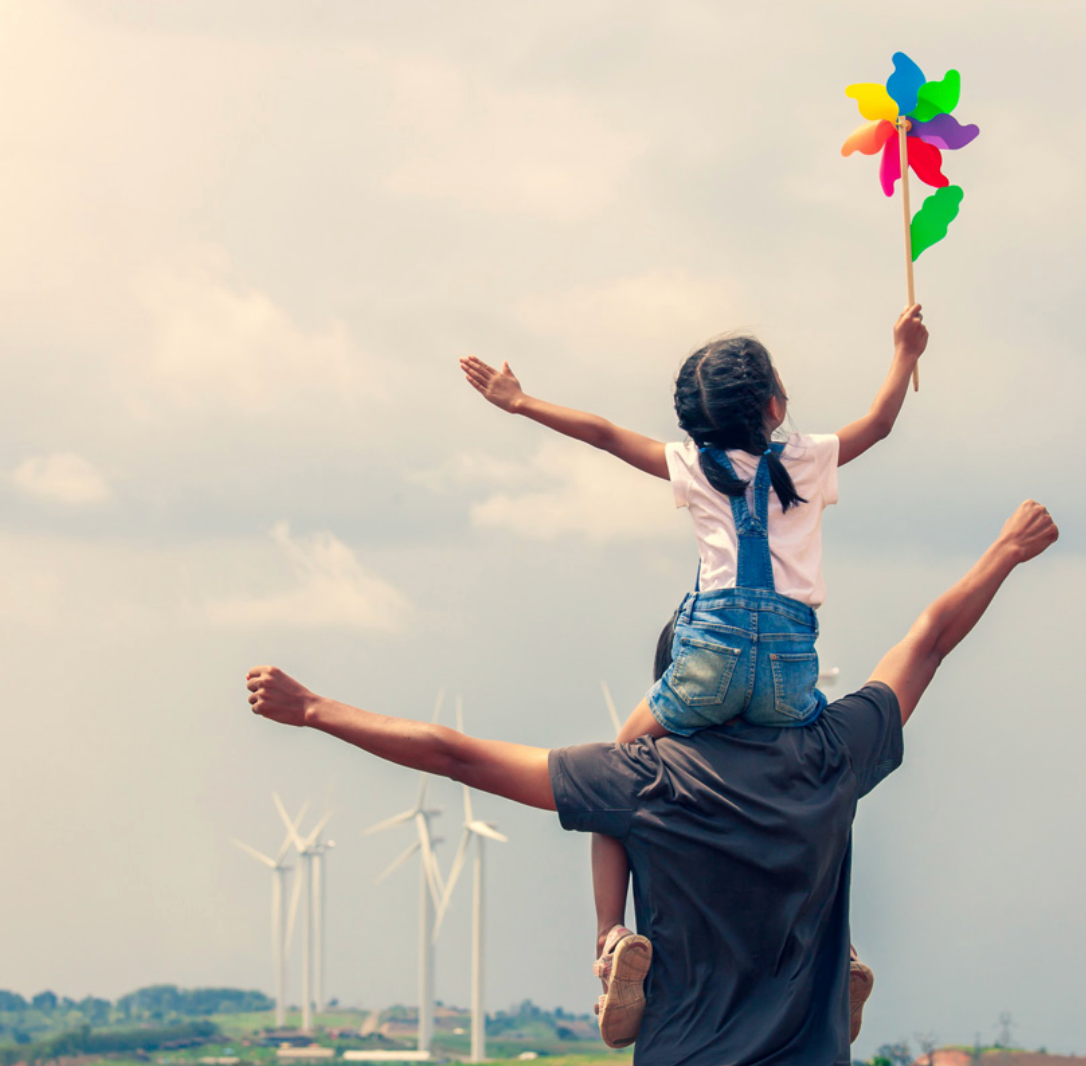 Homme portant sa fille sur les épaules devant des éoliennes