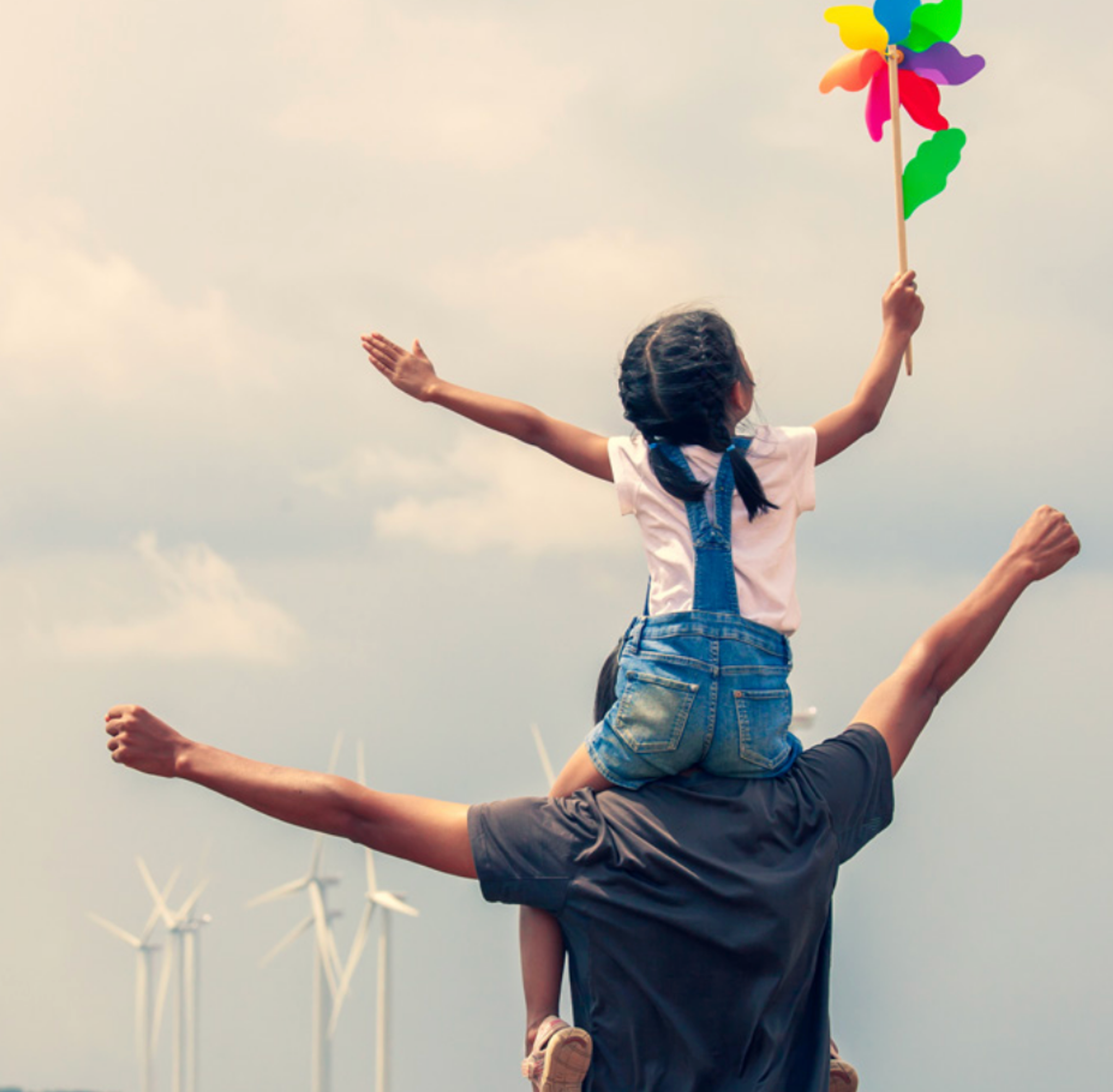 Homme portant sa fille sur les épaules devant des éoliennes