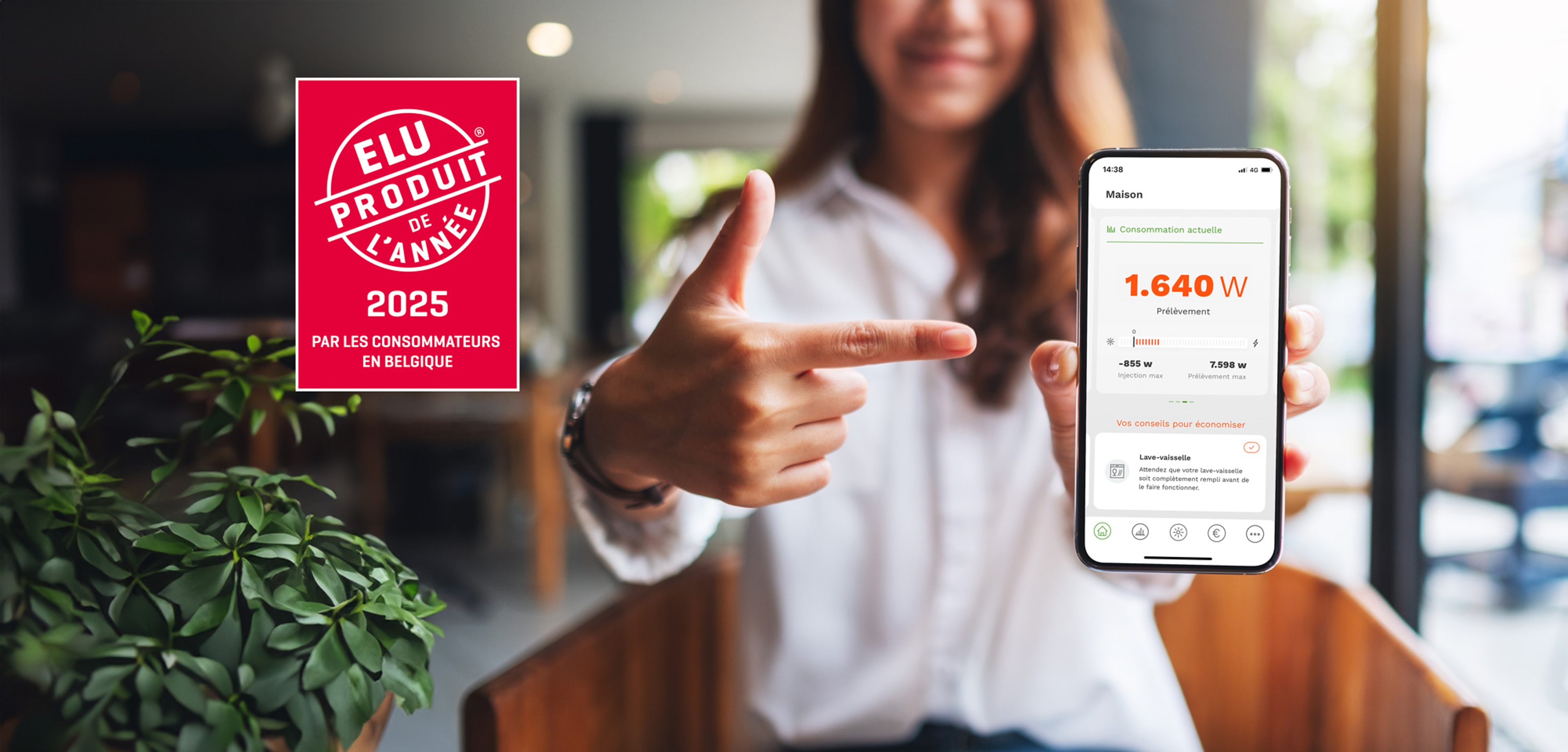 Femme tenant un smartphone affichant une application de suivi de consommation d’énergie, avec un autocollant rouge indiquant ‘Élu produit de l’année 2025 par les consommateurs en Belgique