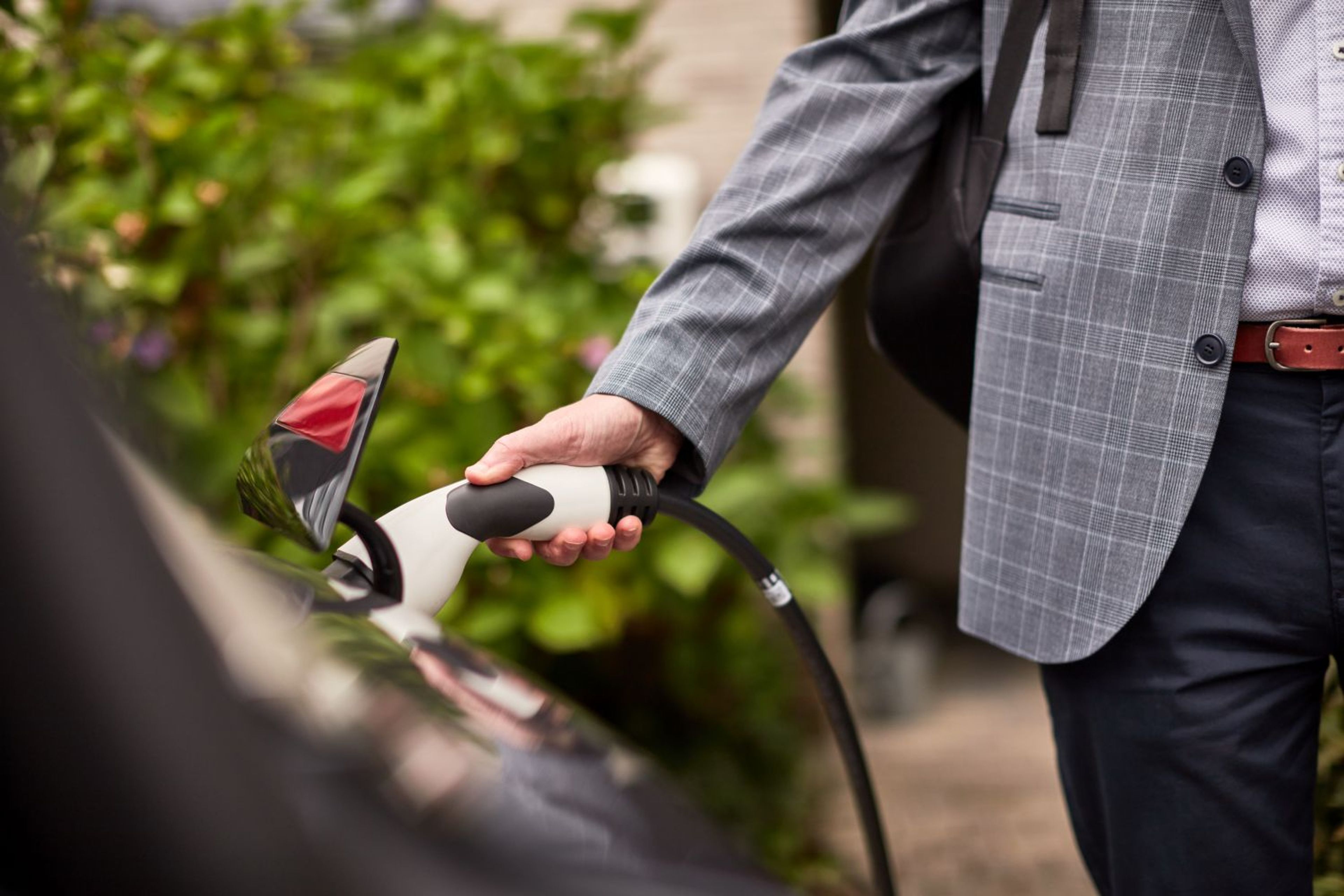 Un homme en costume branche le câble de recharge d'une voiture électrique, illustrant la transition vers la mobilité électrique
