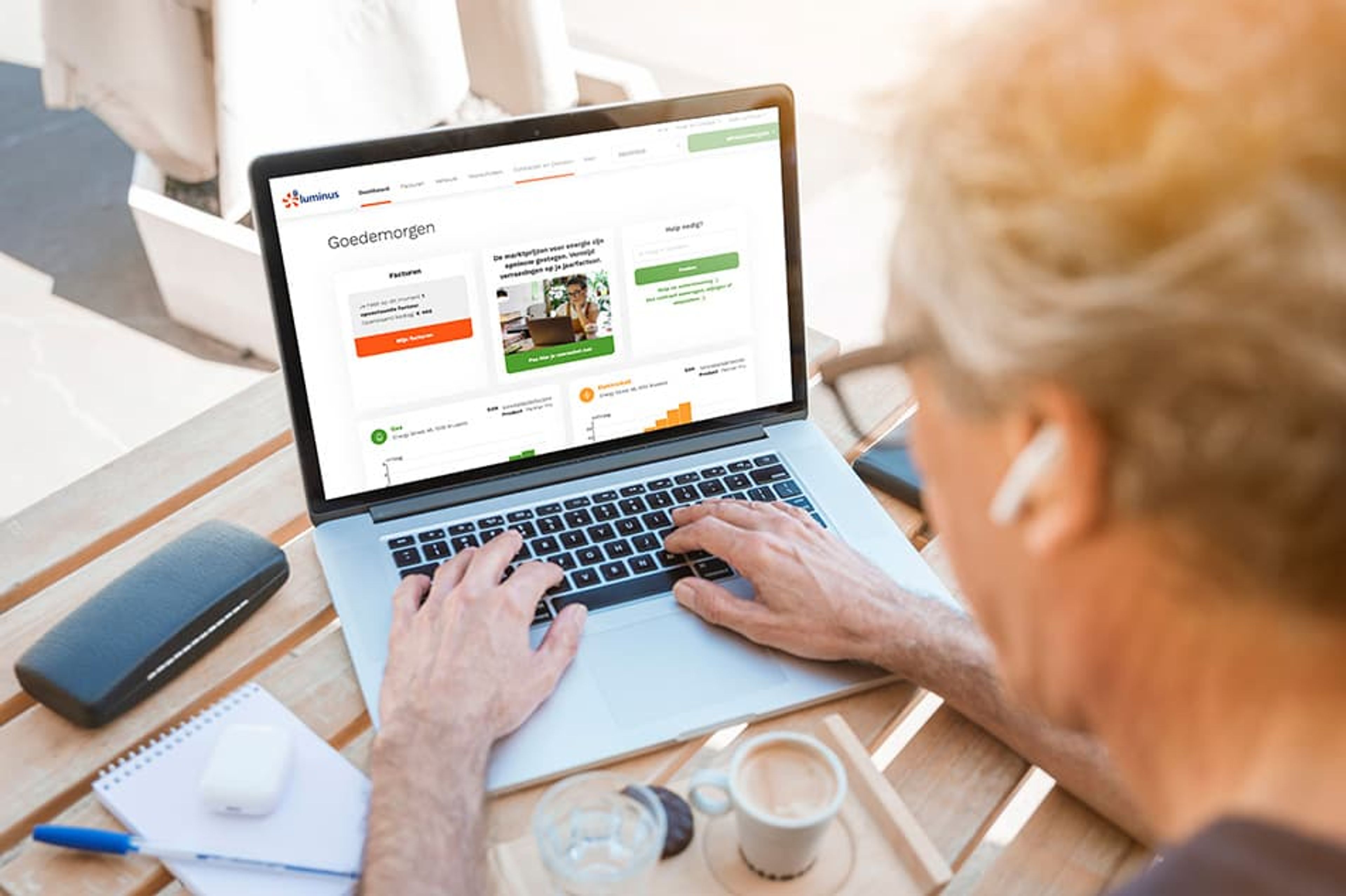 Scherm klantenzone My Luminus: oudere persoon met oortjes in, tokkelt op laptop