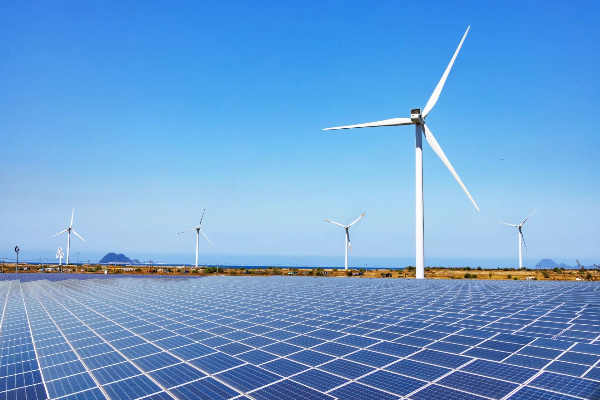 Champ de panneaux solaires avec plusieurs éoliennes en arrière-plan sous un ciel bleu dégagé