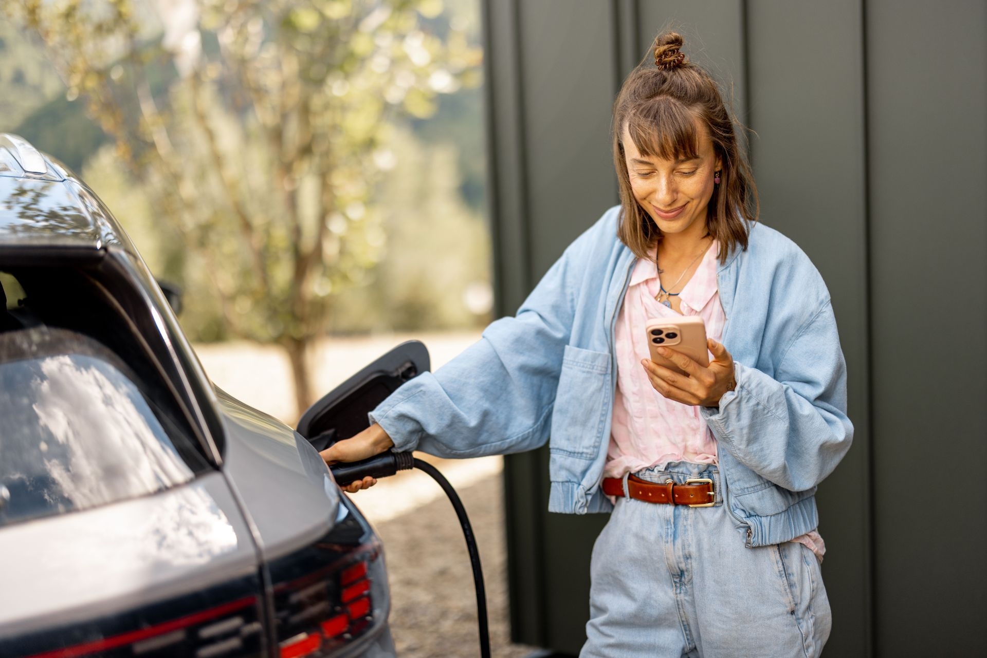 Une jeune femme regarde son téléphone pendant qu’elle branche le câble de recharge de sa voiture