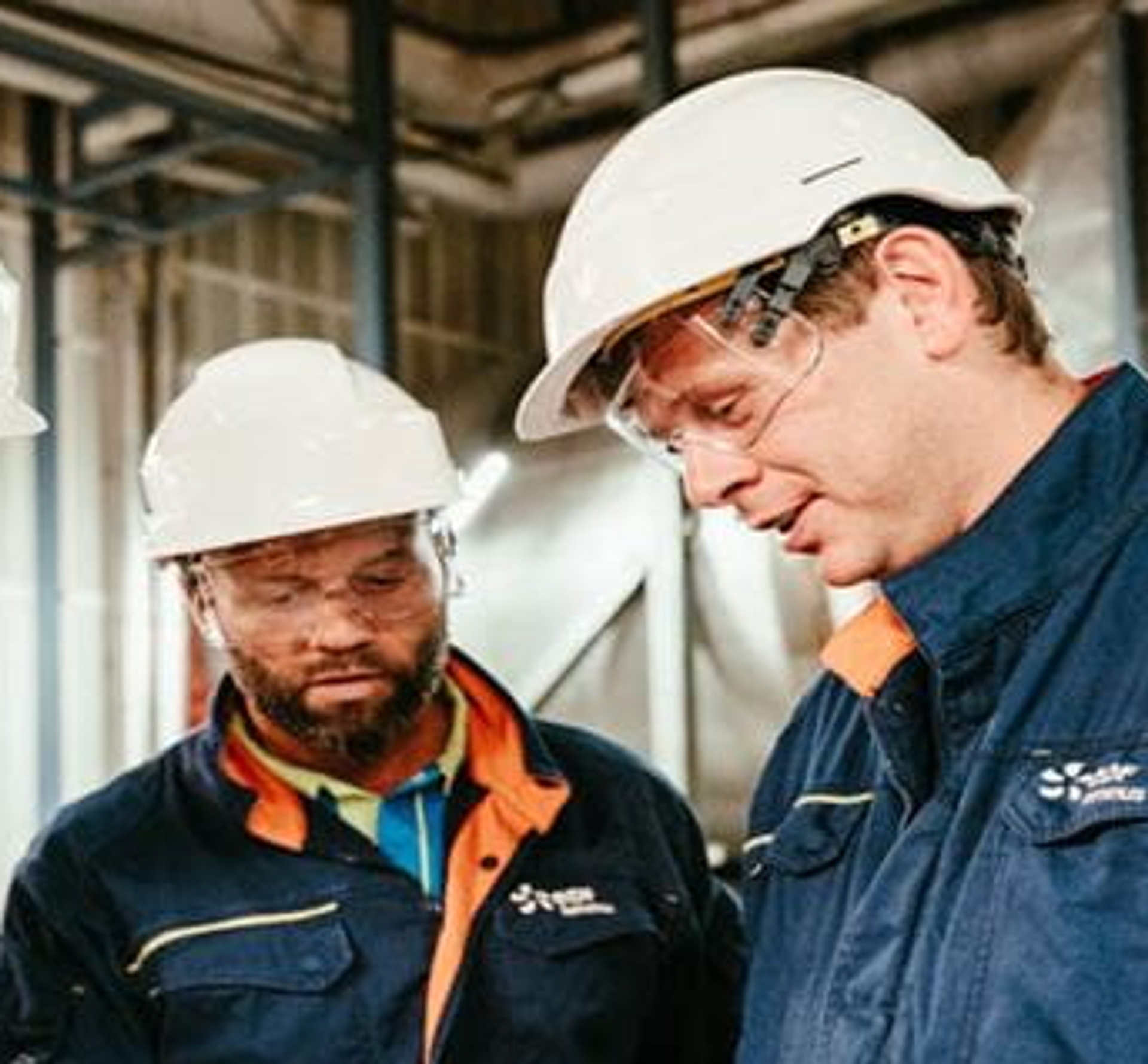 Twee Luminus-techniekers met witte helm op bekijken iets samen in een centrale.