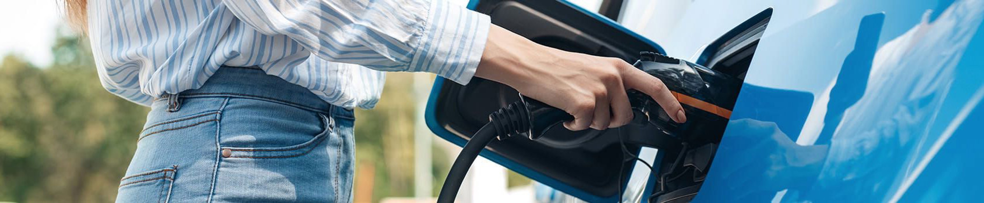 Personne en chemise rayée et jean branchant un câble de recharge sur une voiture électrique