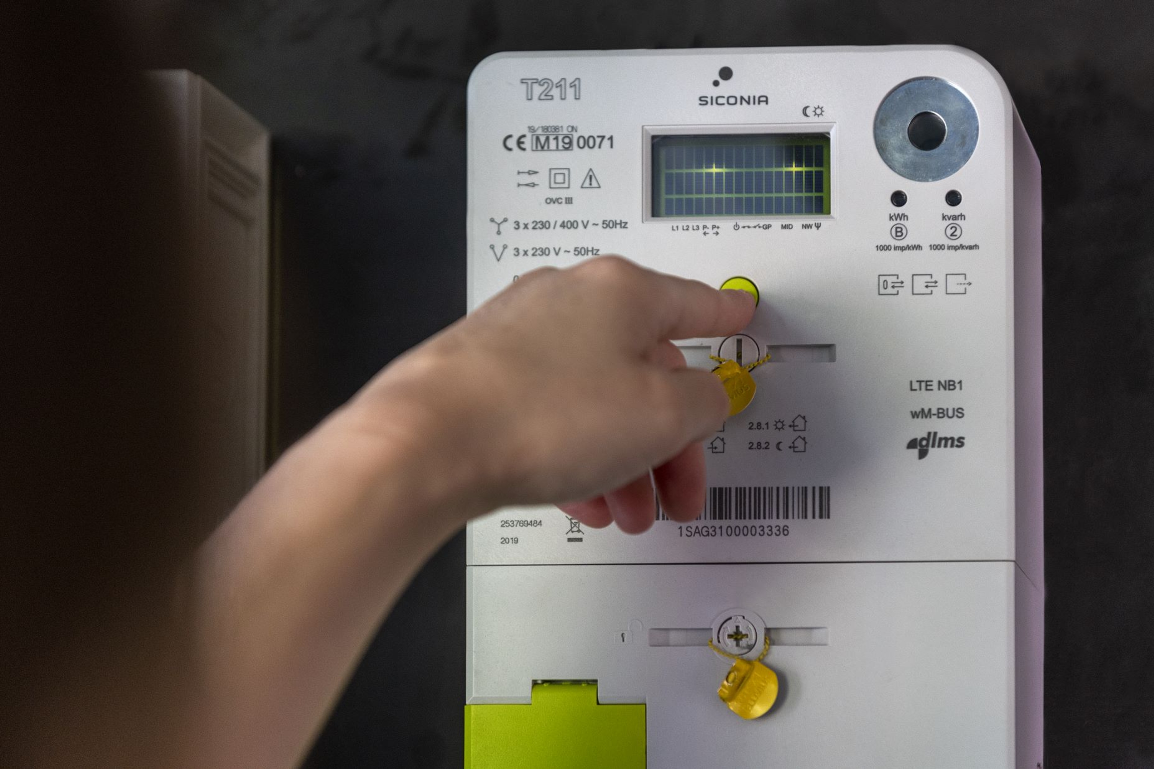Gros plan sur une main réglant un compteur électrique intelligent, avec écran numérique affichant des données de consommation
