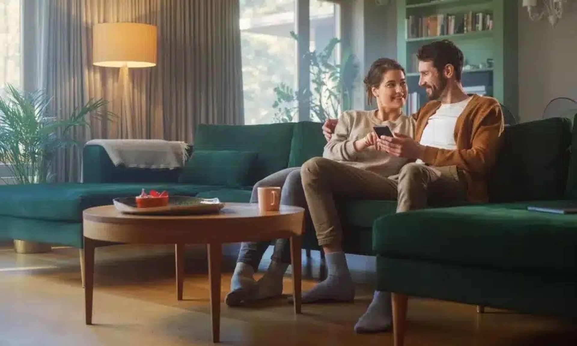 Couple assis sur un canapé dans un salon moderne, partageant un moment complice avec un smartphone à la main