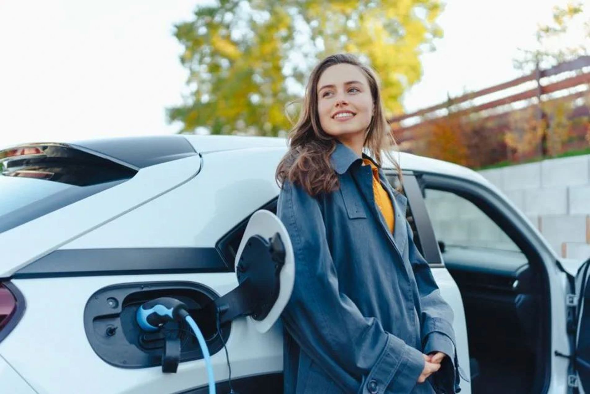 Jongedame met oker top bij haar elektrische wagen die aan het opladen is.