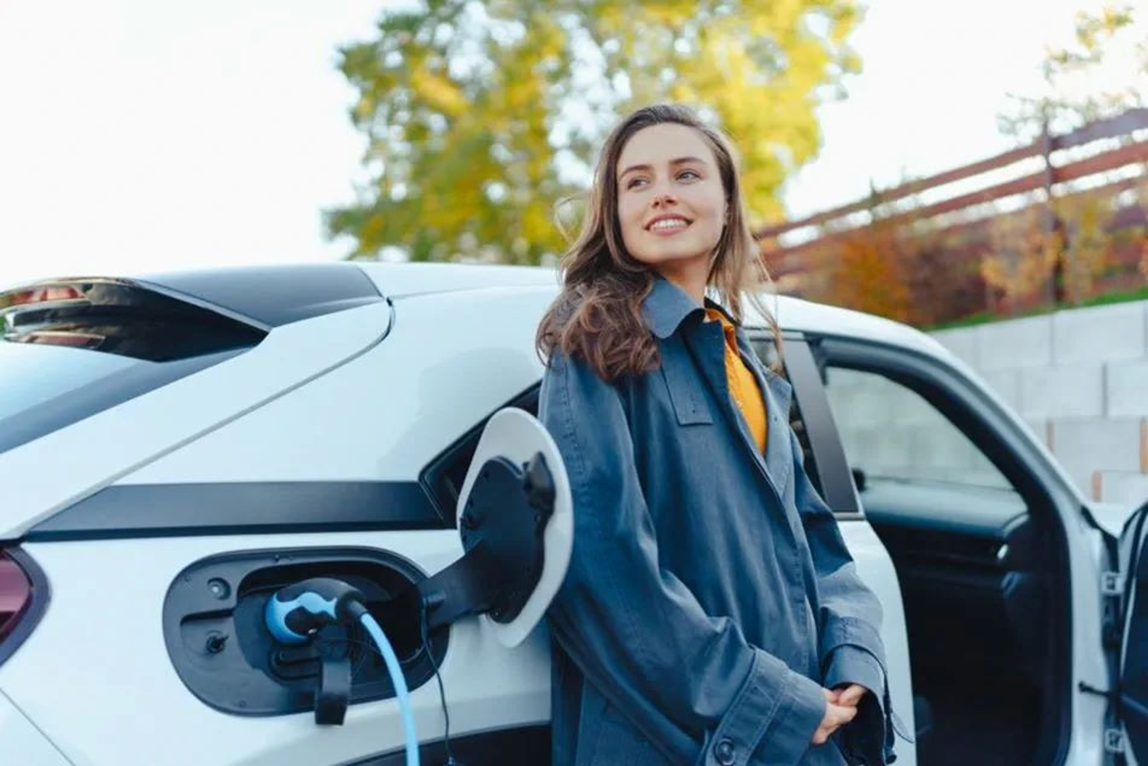 jonge vrouw staat lachend bij haar elektrische wagen die aan het opladen is