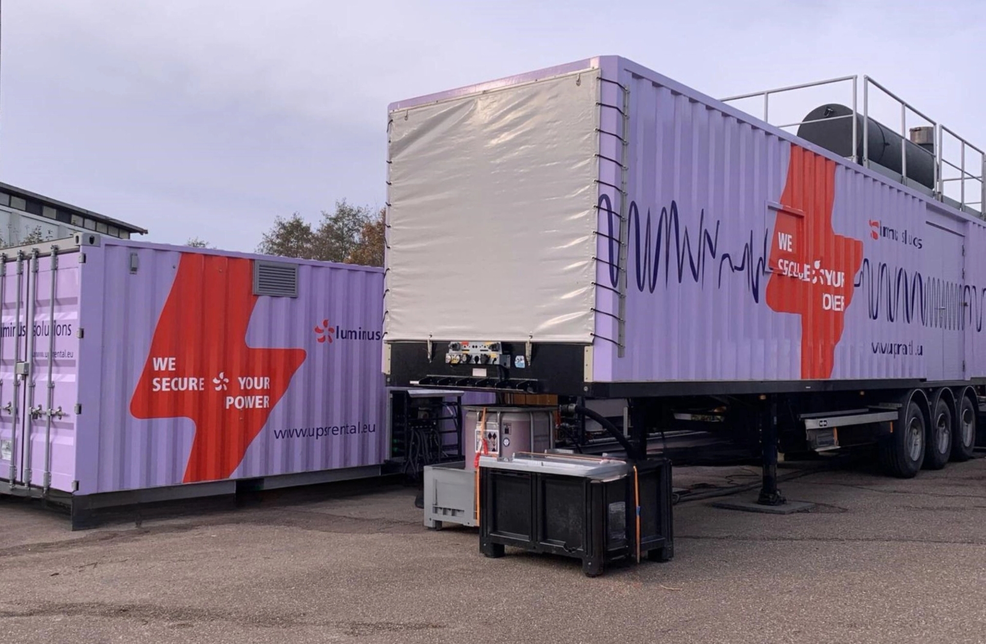Uninterruptible Power Supply - Twee mobiele Luminus-containers, voorzien van de slogan "Wij beveiligen uw stroom", geïnstalleerd op een industriële site