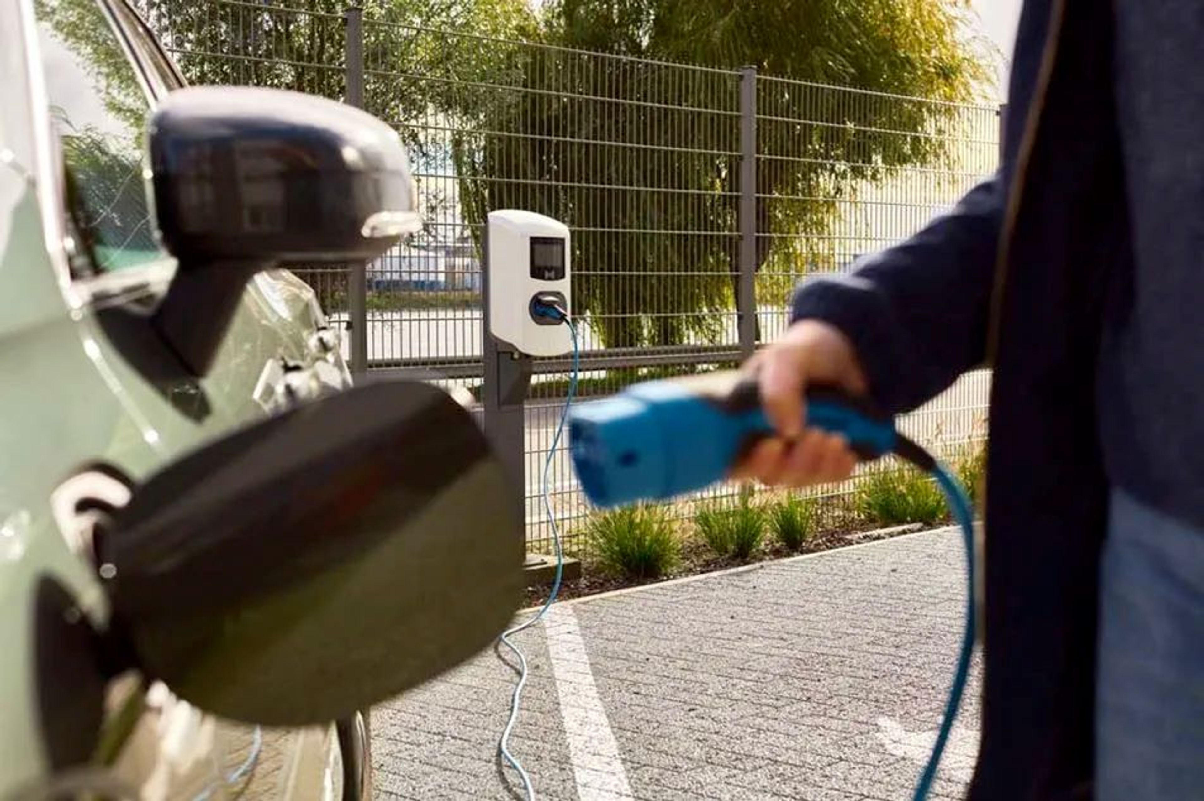 Man gaat net de stekker insteken om zijn groene elektrische wagen op te laden aan een openbare laadpaal.