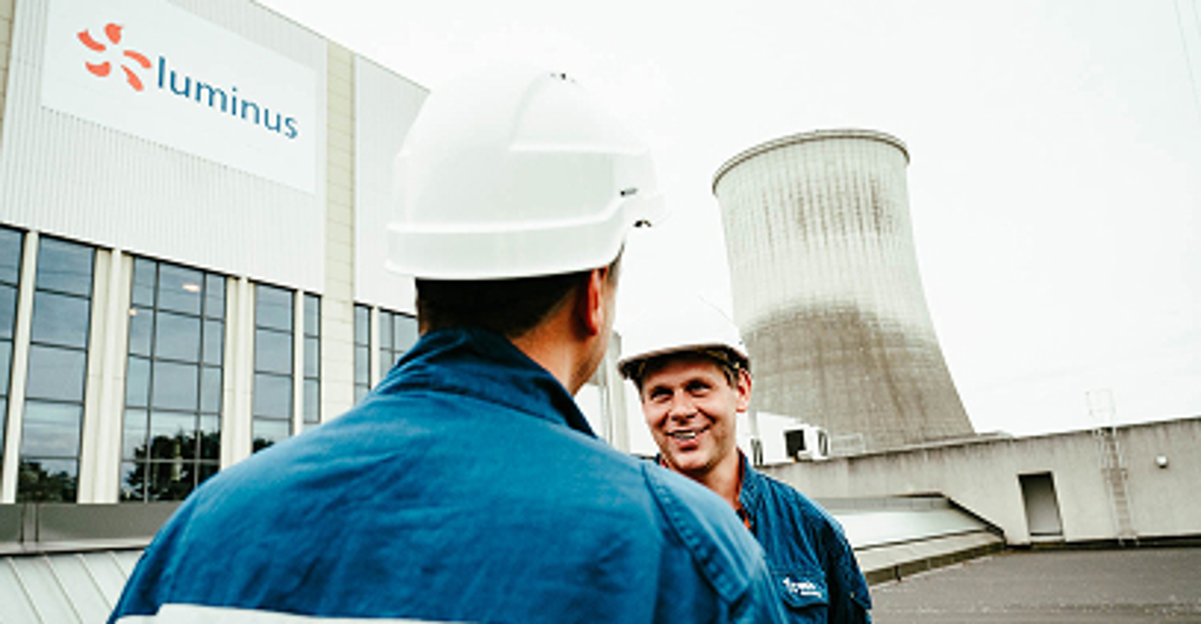 2 Luminus technici met witte helm op, koeltoren op de achtergrond.