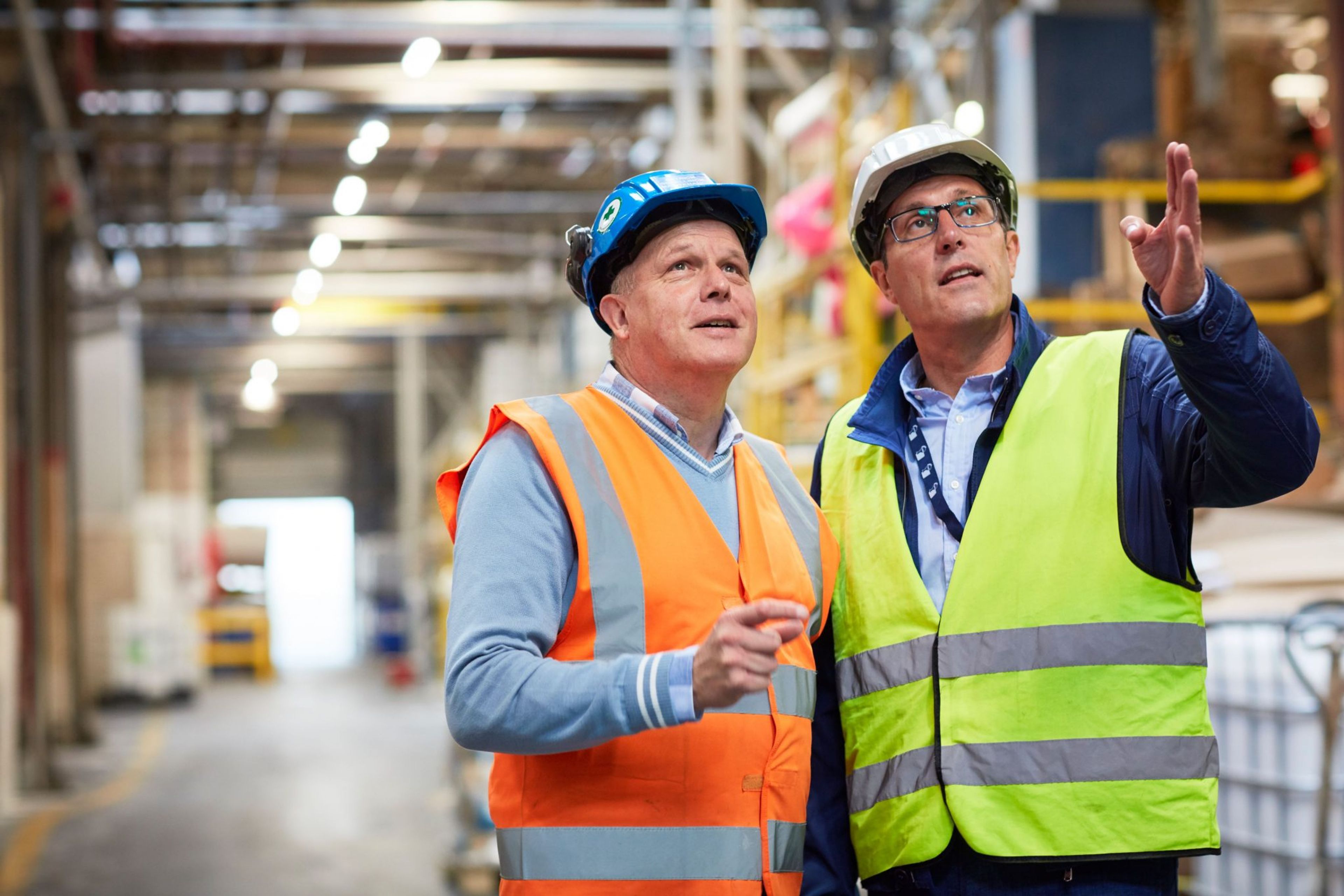 Deux ingénieurs portant des casques et des gilets fluorescents discutent dans un entrepôt industriel