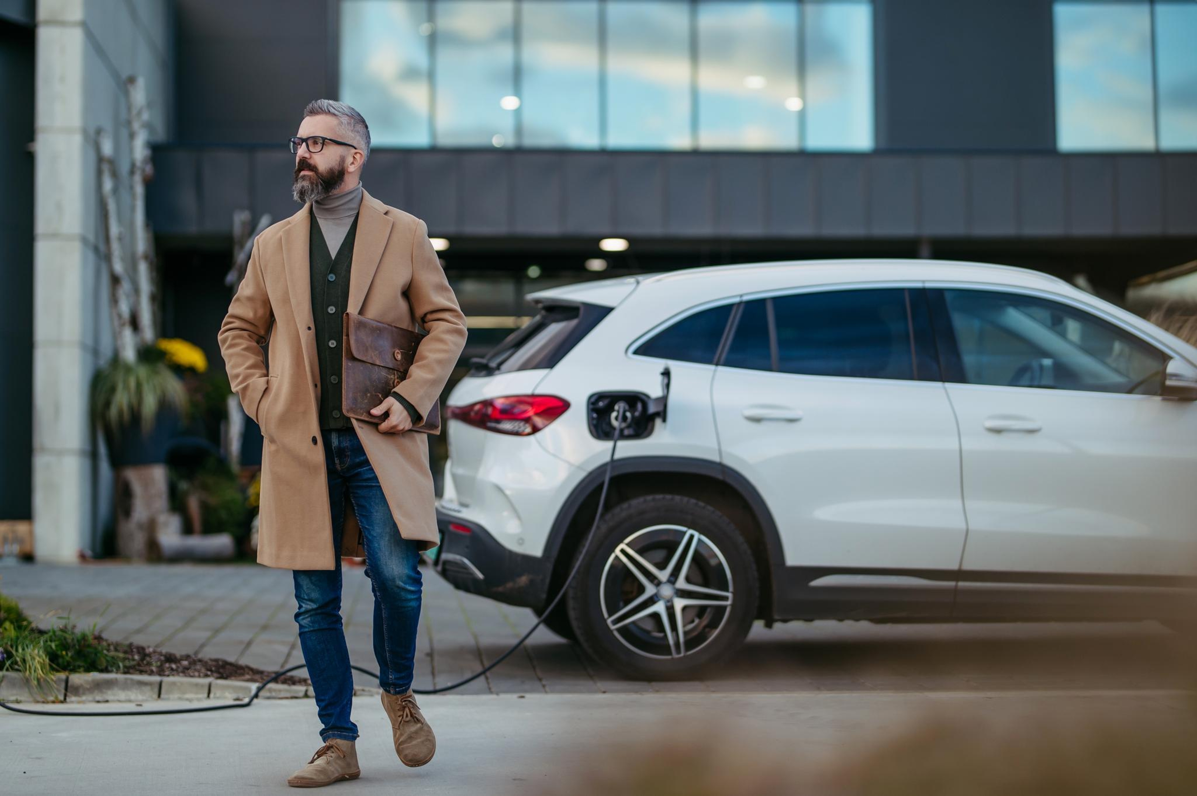 Un homme en tenue professionnelle décontractée recharge sa voiture électrique avant d'aller travailler.
