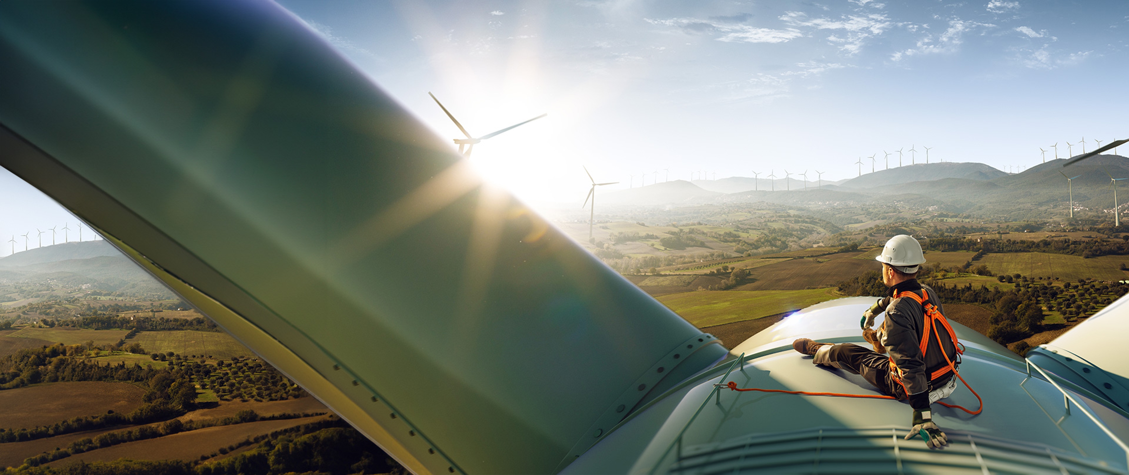 Persoon met helm zit beveiligd bovenop een windturbine